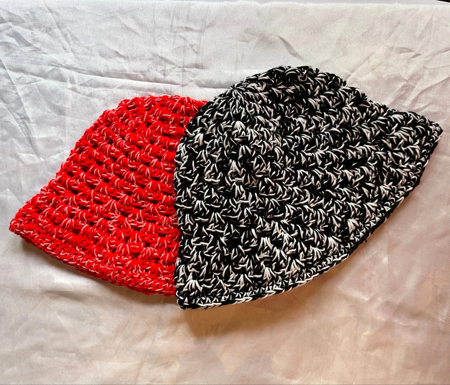 Two crochet hats, one red and one black and white patterned, on a textured surface.