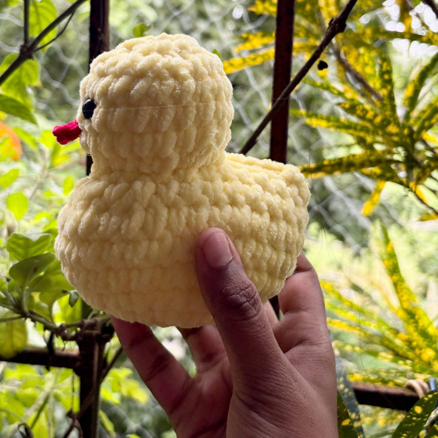 Hand holding a yellow crochet duck toy with a blurred green outdoor background