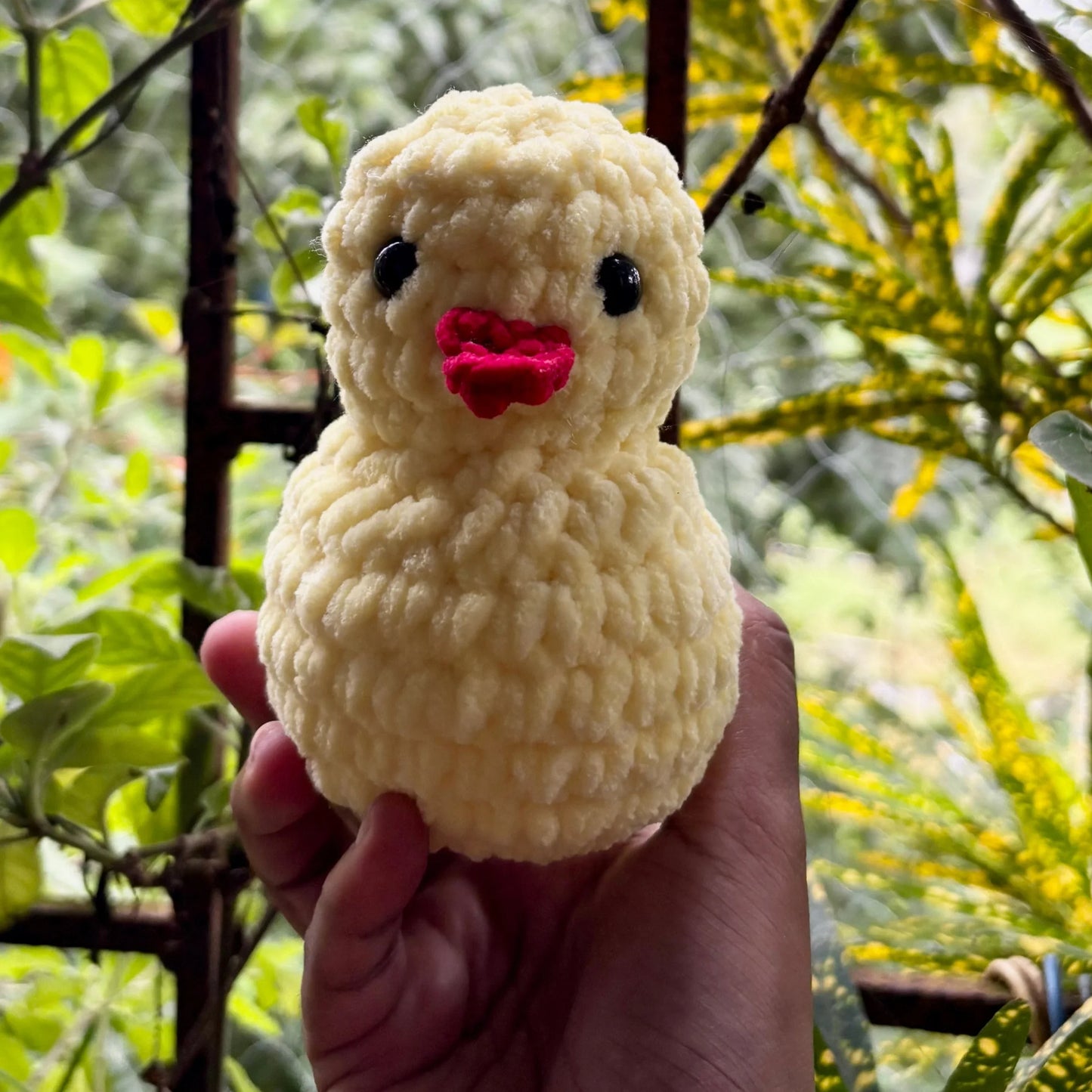 Hand holding a small yellow duck plush toy with a pink beak against a natural background.