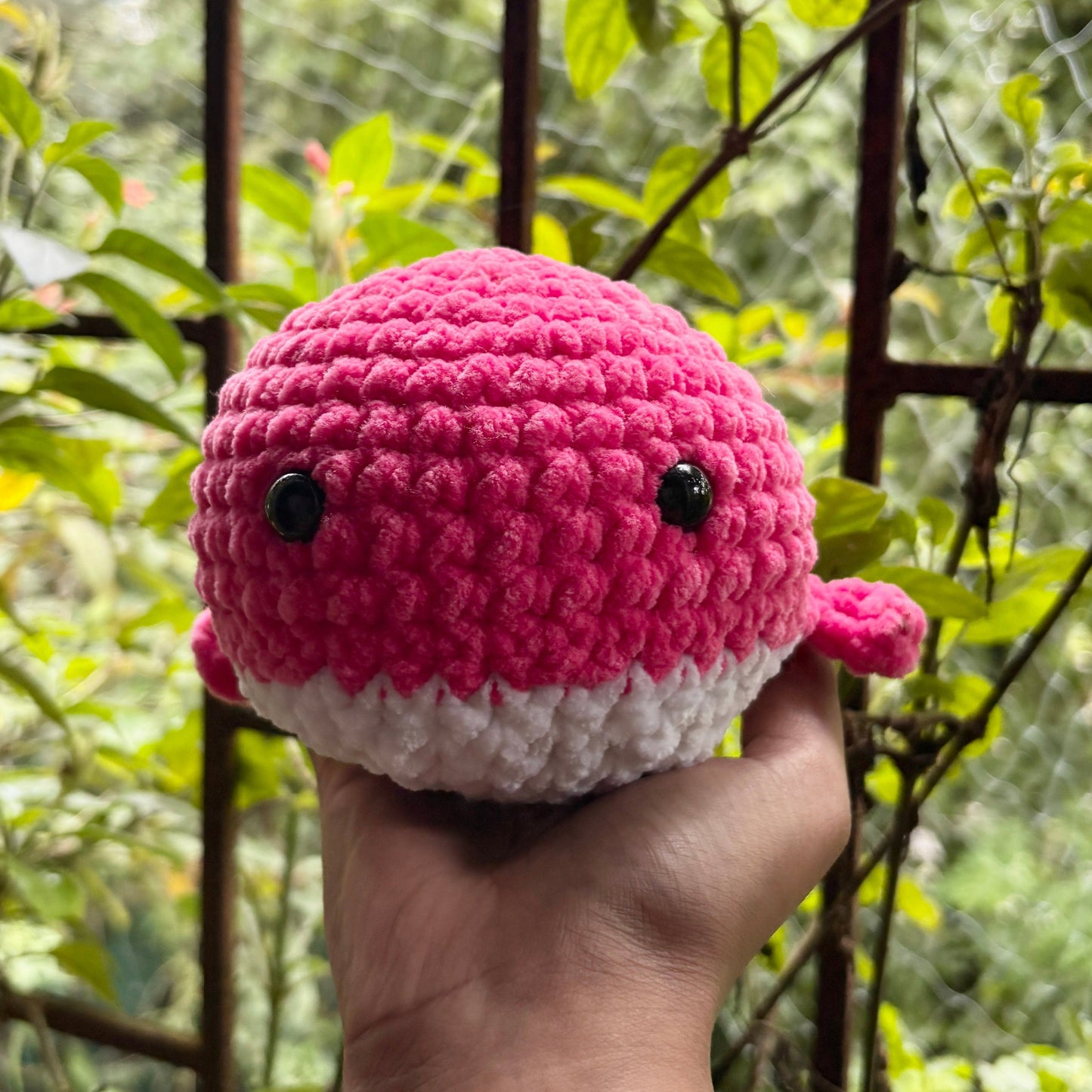 Crocheted pink and white whale held in a hand with a blurred green background