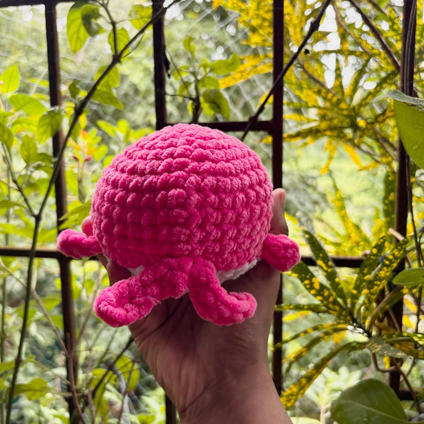 Hand holding a pink crochet whale against a natural background