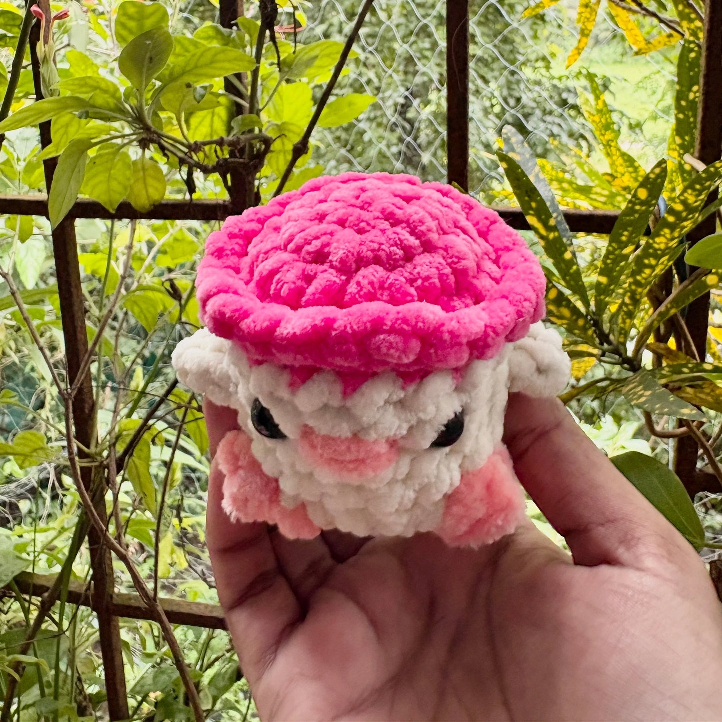 Hand holding a pink and white crochet toy against a natural background