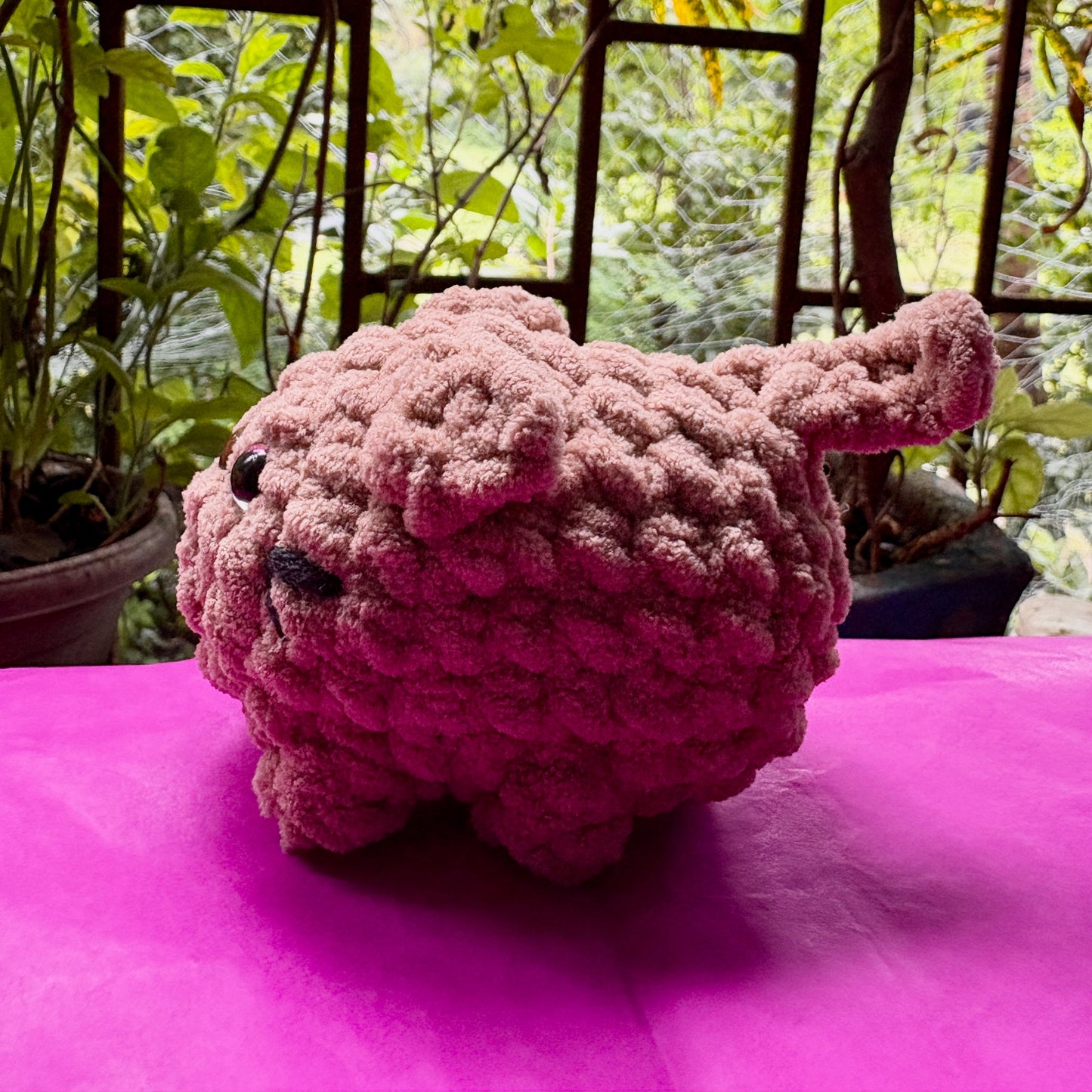 Pink knitted toy on a pink surface with a garden background
