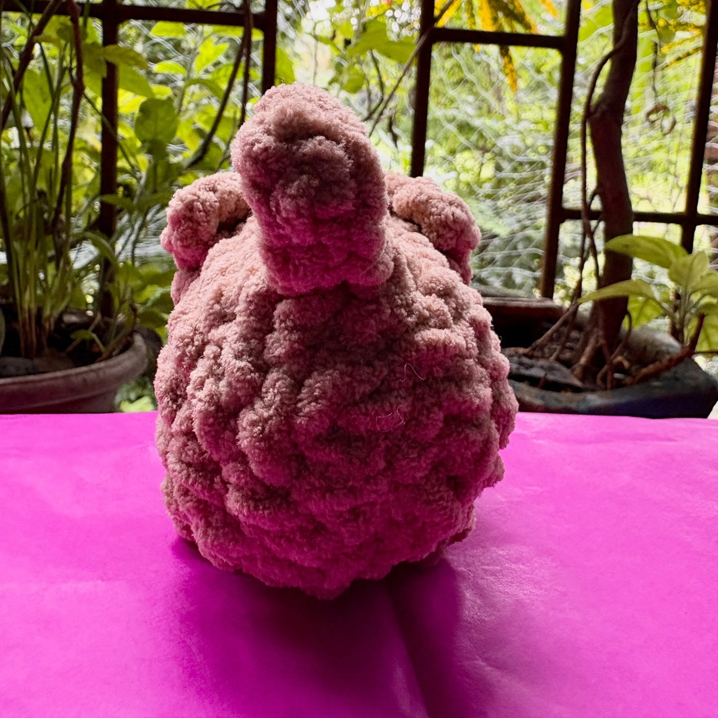 Pink knitted bear on a pink surface with a blurred green outdoor background