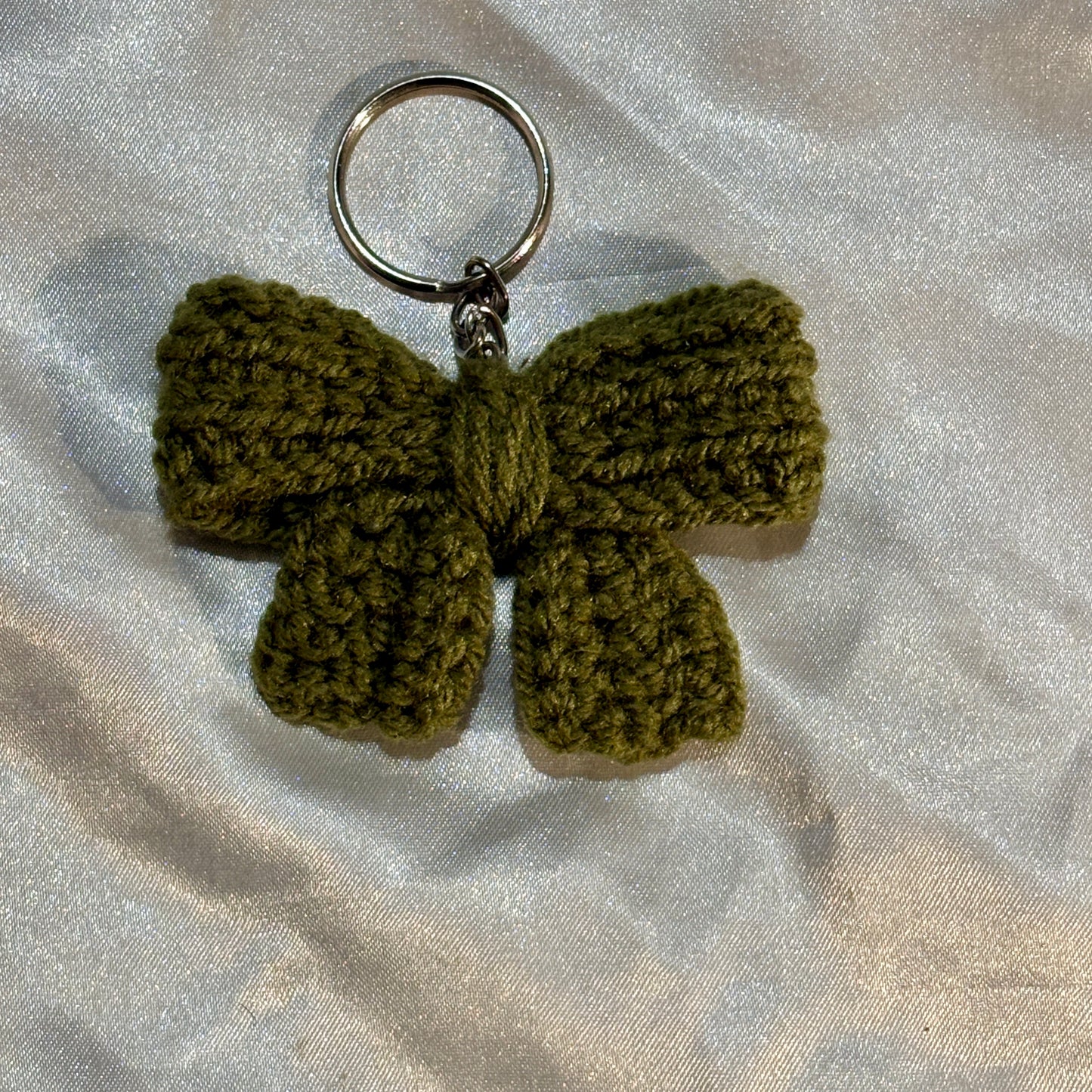Green crocheted bow keychain on a light gray fabric background