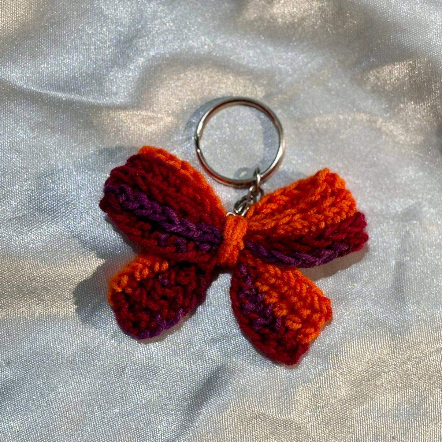 Crocheted bow keychain on a textured silver background