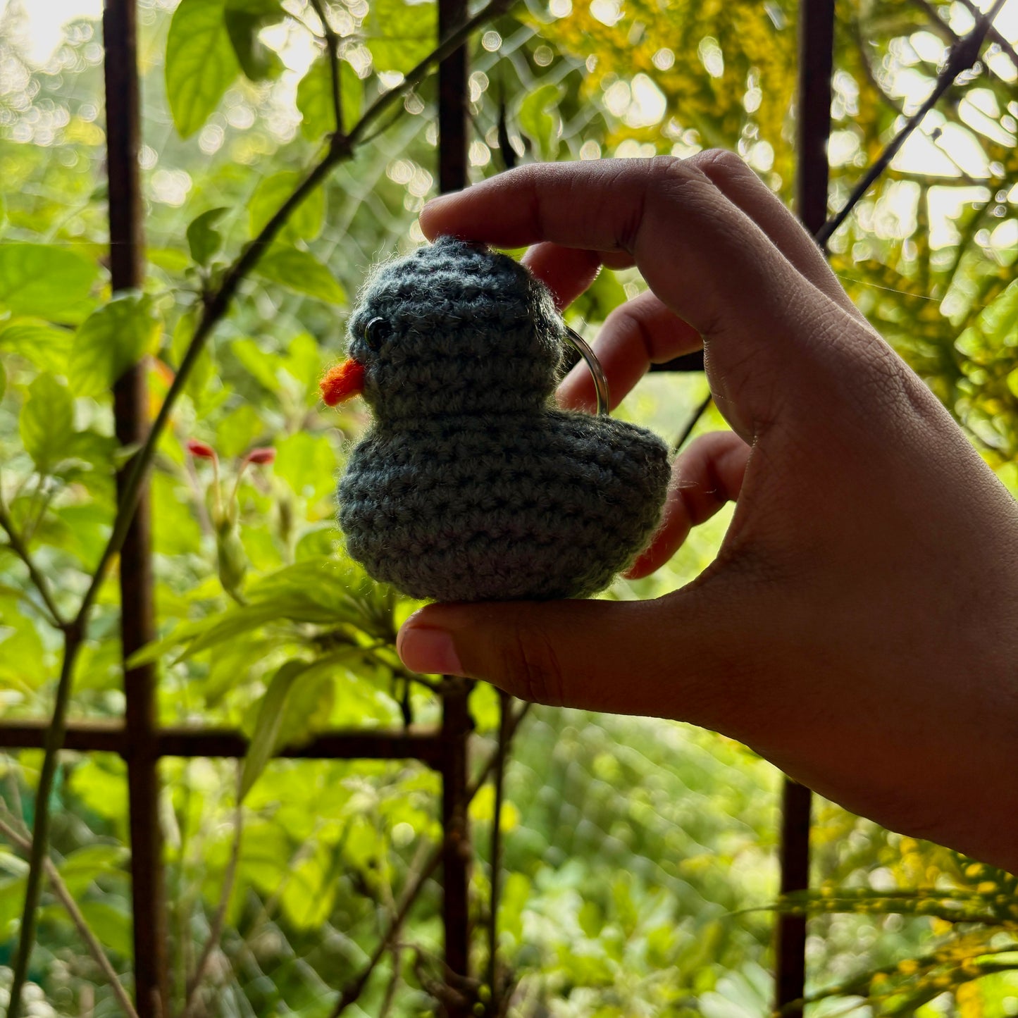 Hand holding a small crocheted bird against a natural background