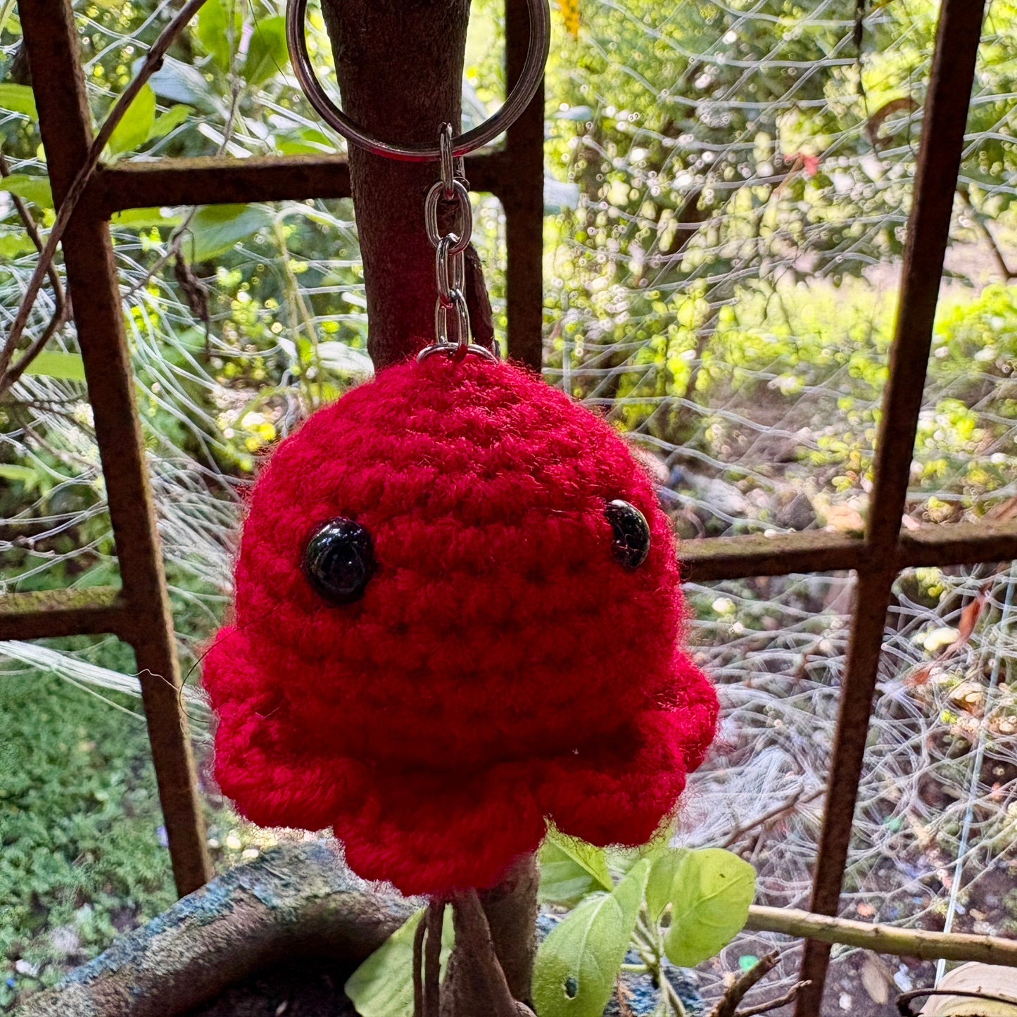 Red crocheted keychain with black buttons hanging on a metal fence.