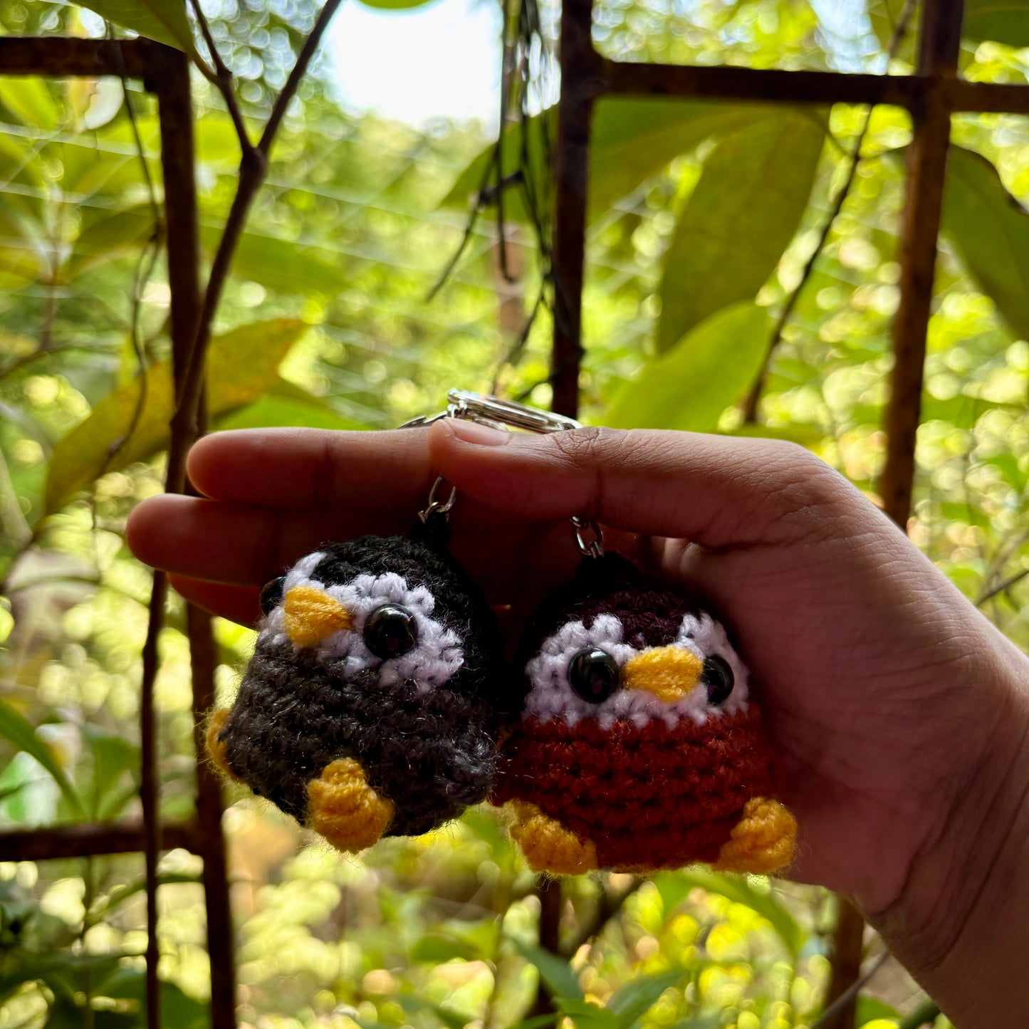 Hand holding two small crocheted penguin keychains with a natural background