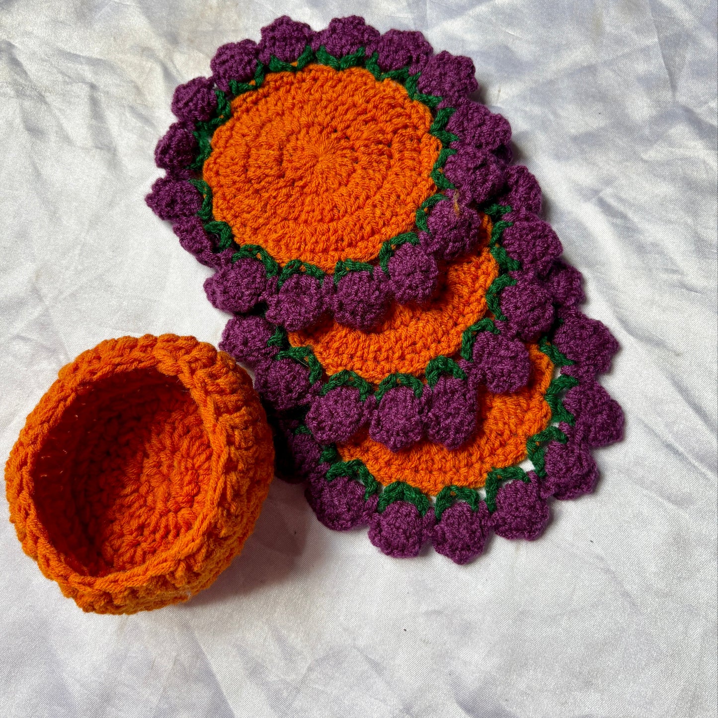Set of purple and orange crocheted coasters on a white surface