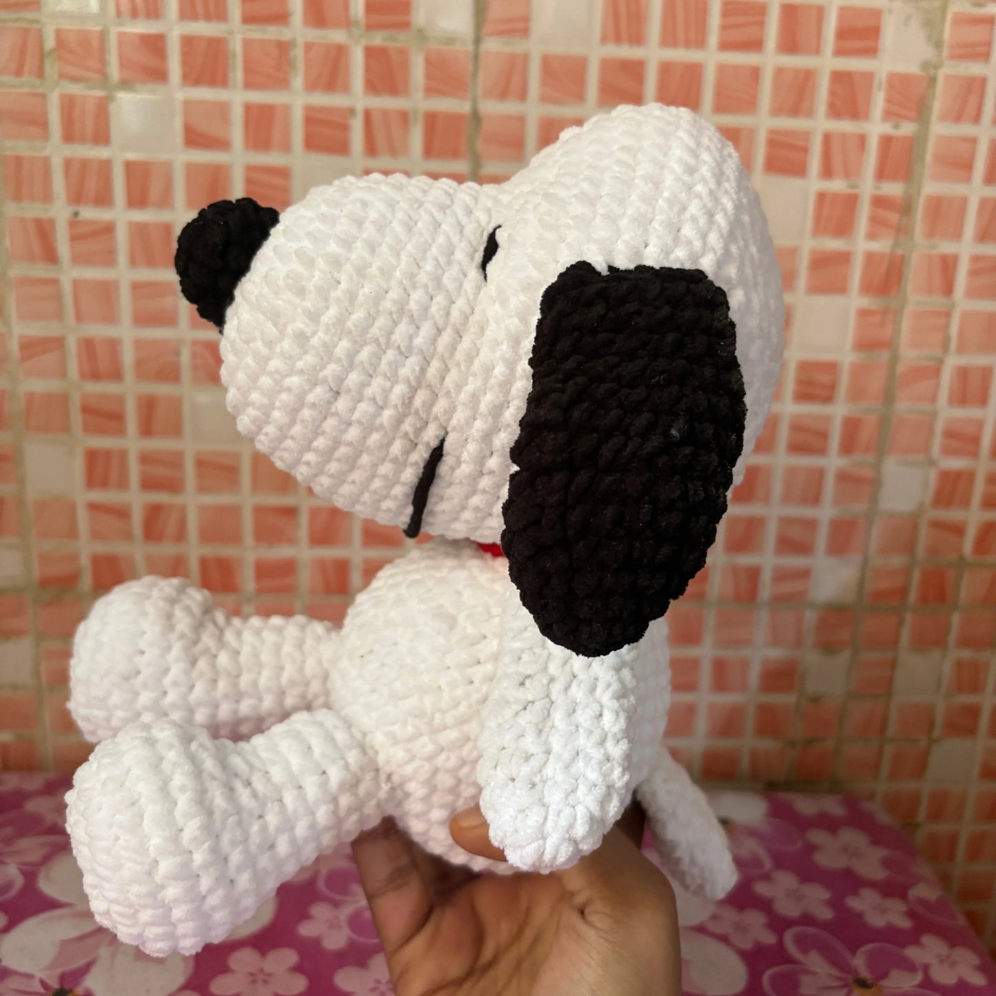 Handmade crochet dog toy held by a person against a tiled wall background