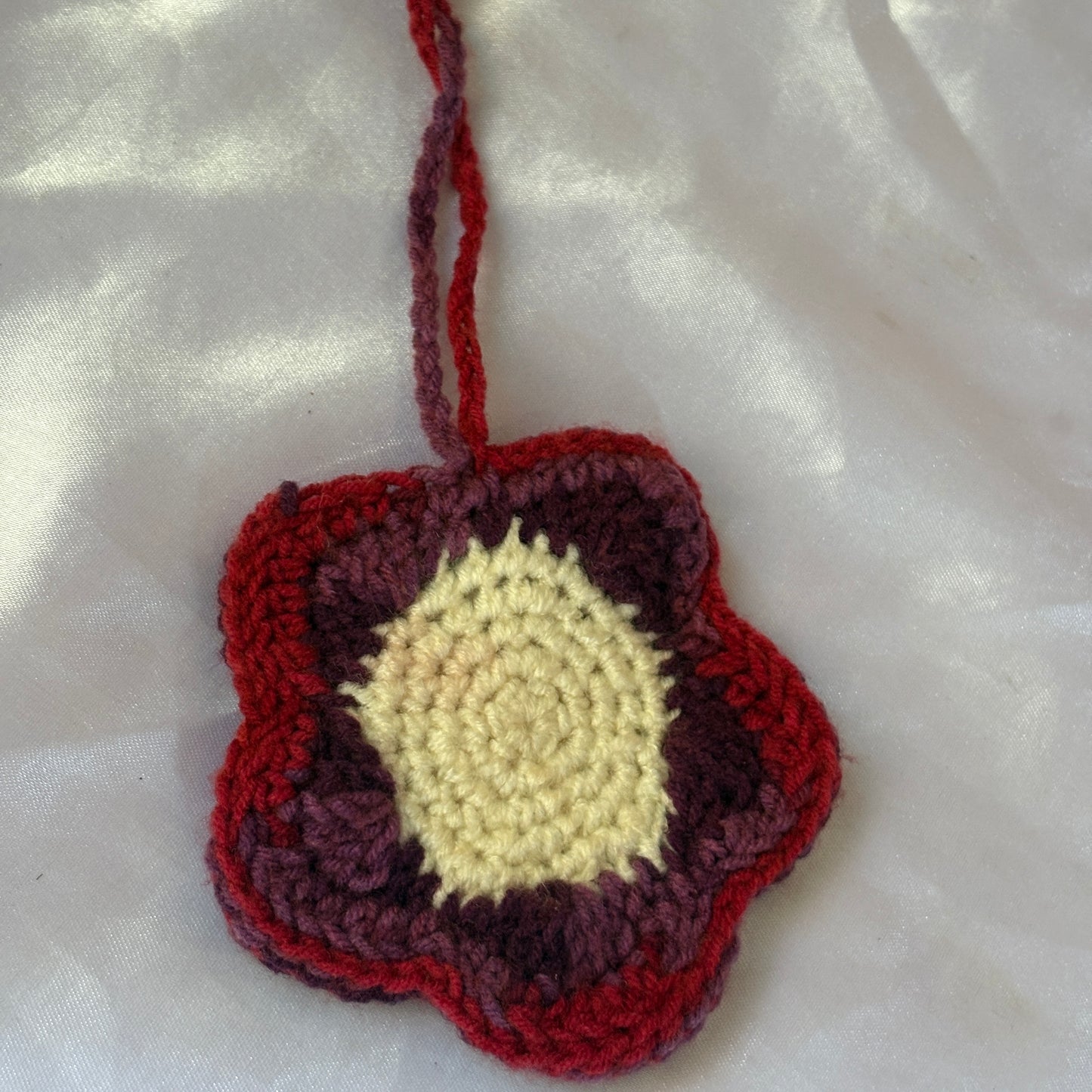 Crocheted flower-shaped pouch with red, purple, and beige colors on a white fabric background