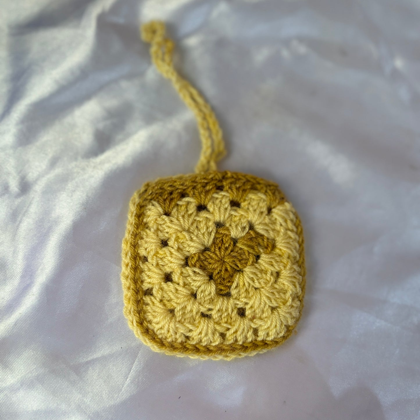 Yellow crocheted square on a white fabric background
