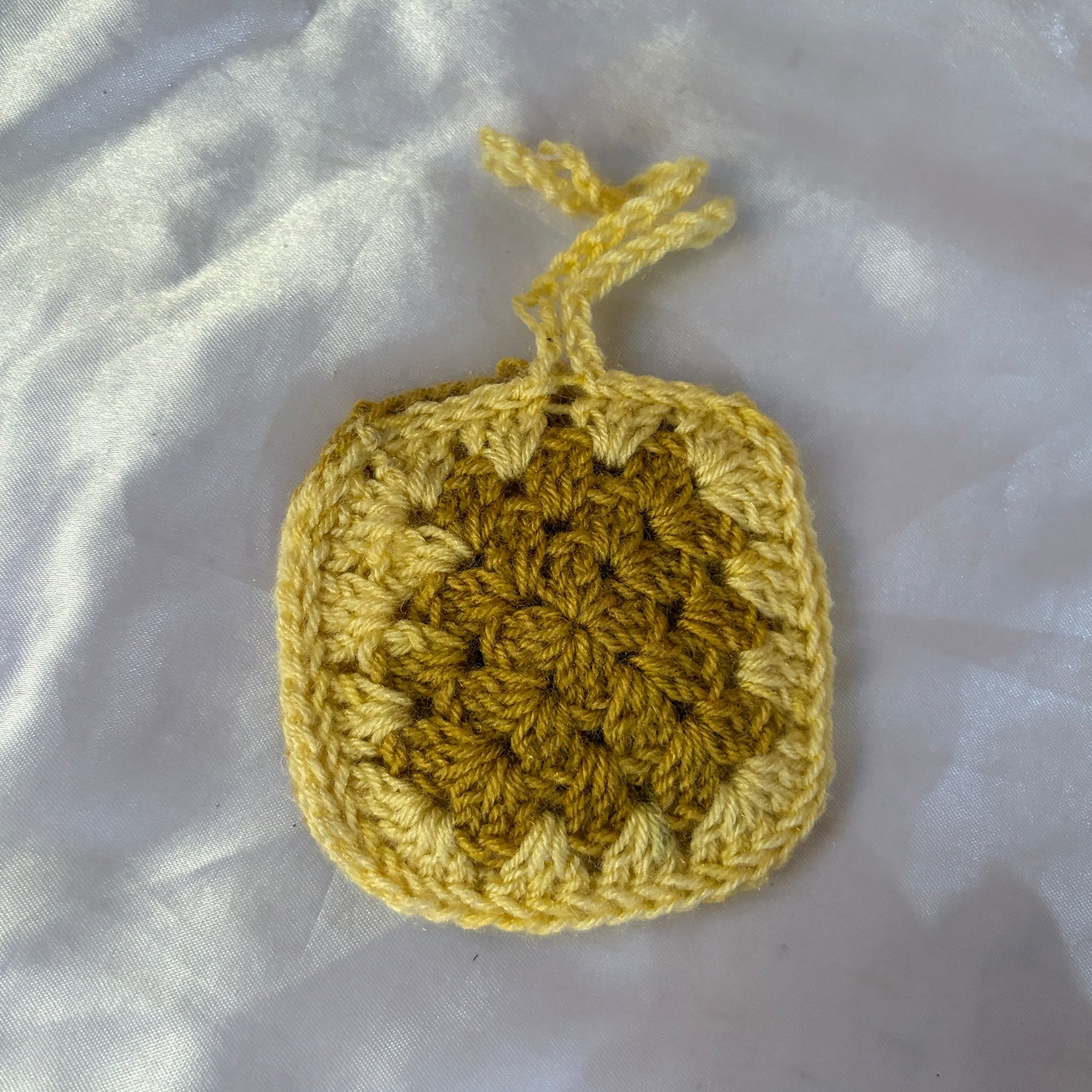 Crocheted yellow square on a white fabric background