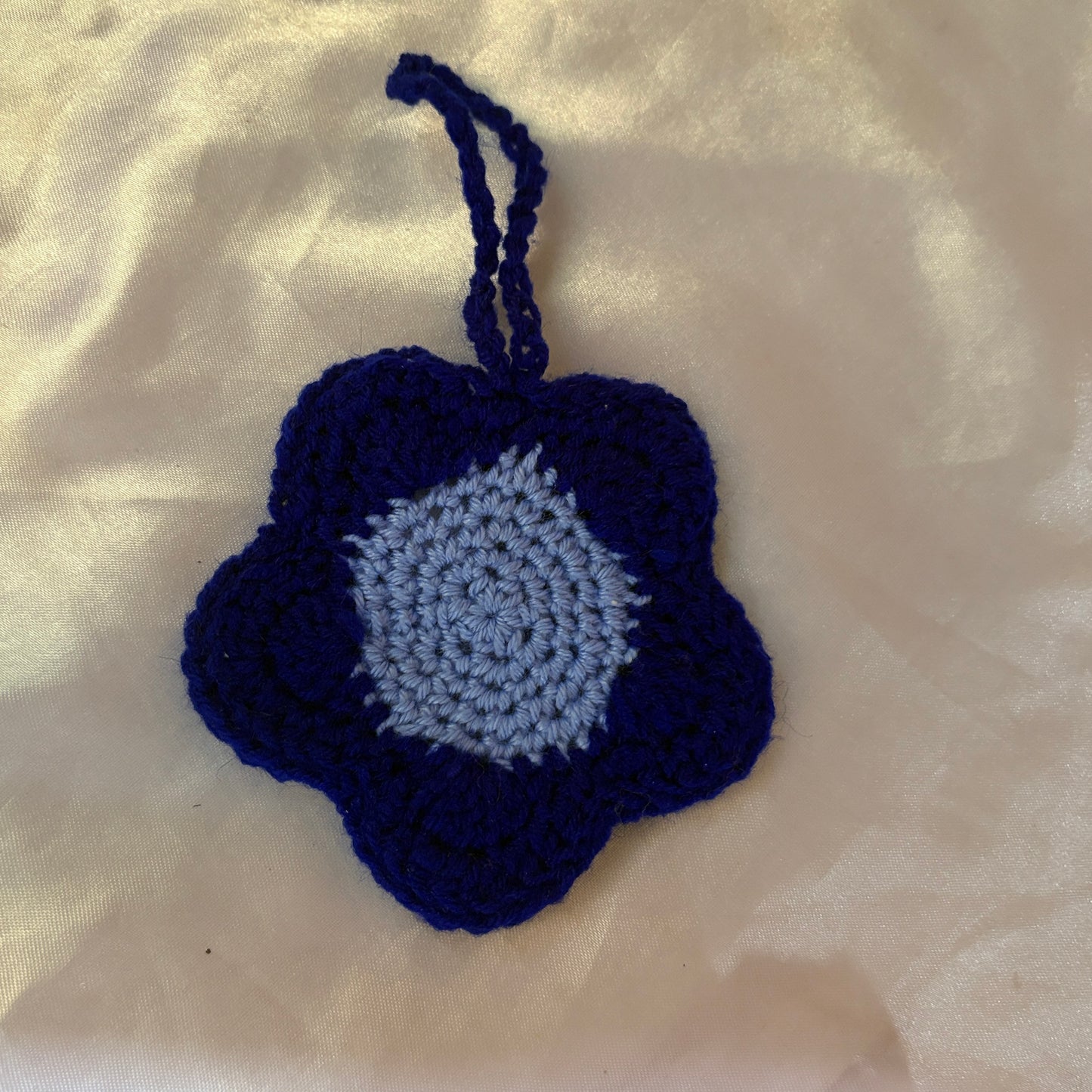 Crocheted flower-shaped pouch with blue and gray colors on a beige fabric background