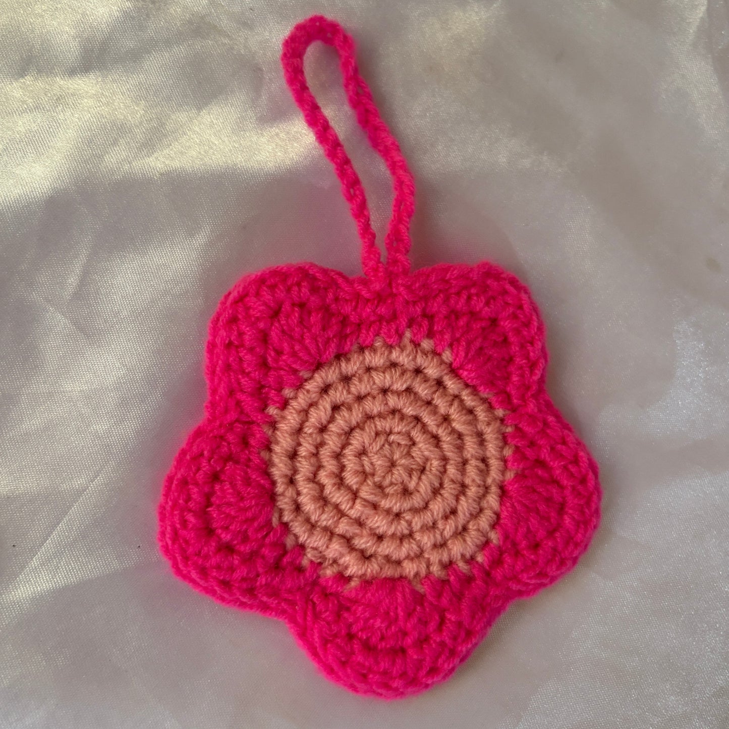 Crocheted pink flower with a light pink center on a light fabric background