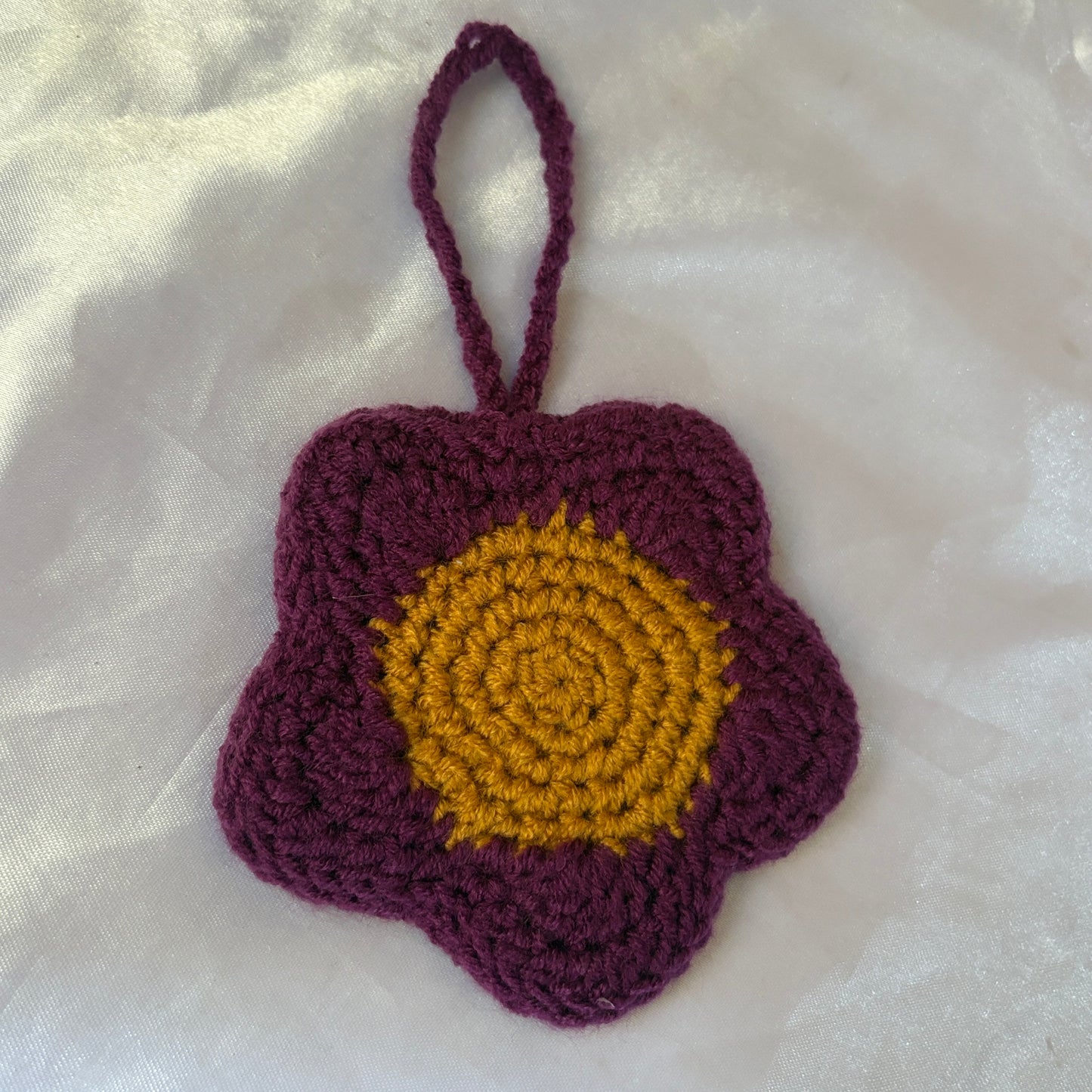 Crocheted flower pouch with purple petals and yellow center on a white fabric background