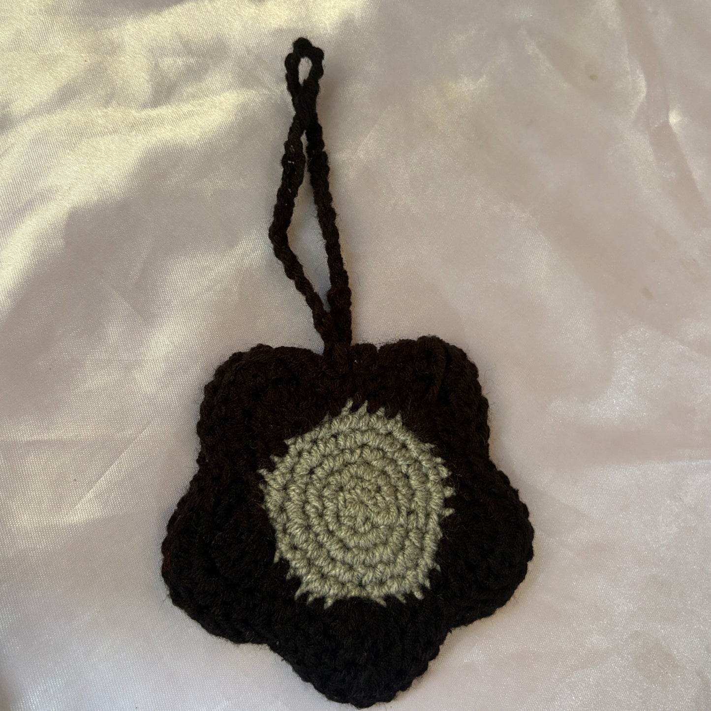 Crocheted black and green flower-shaped pouch on a light fabric background