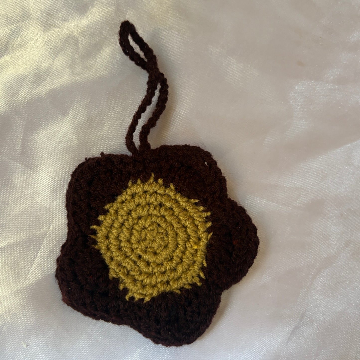 Crocheted item with brown border and green center on a light fabric background