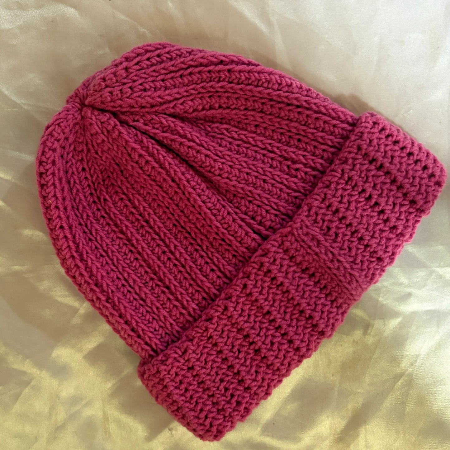 Pink crochet beanie on a light beige fabric background