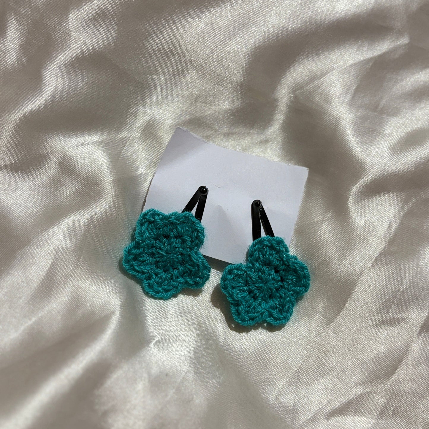 Teal crocheted black clips on a white fabric background