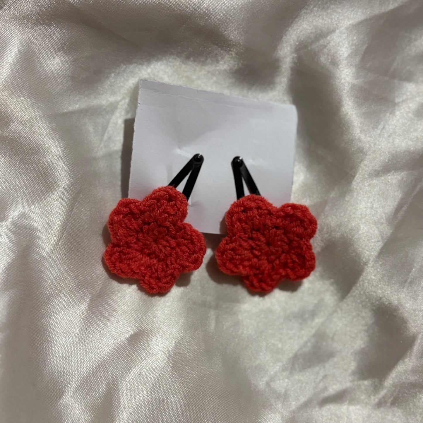 Red crocheted star hair clips on a white card with a white fabric background