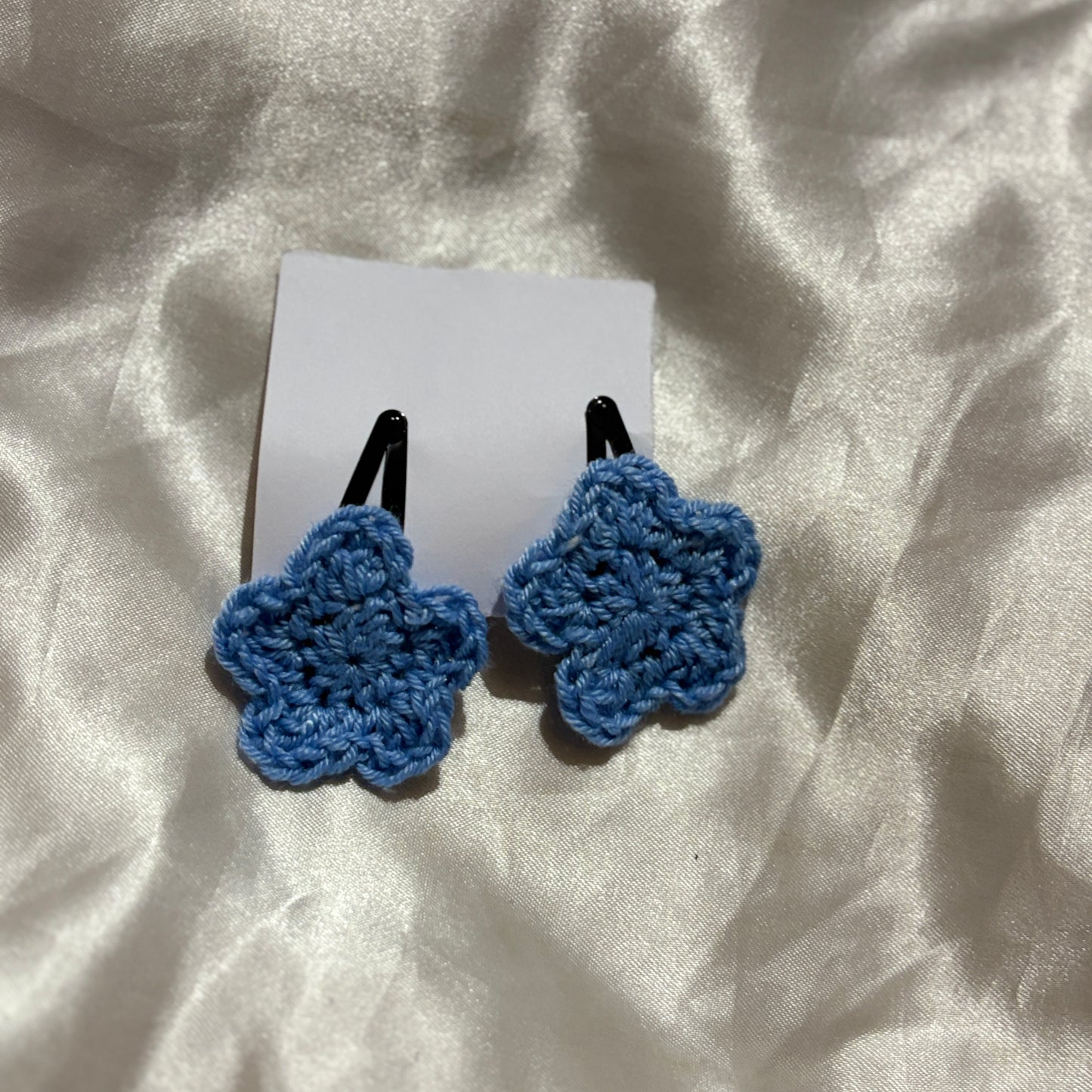 Blue crocheted hair clips on a white card with a white fabric background