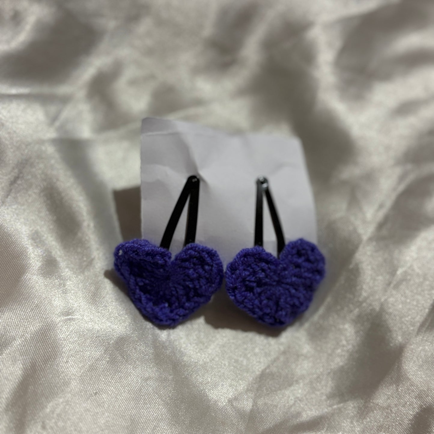 Pair of blue heart-shaped hair clips on a white card with a textured beige background