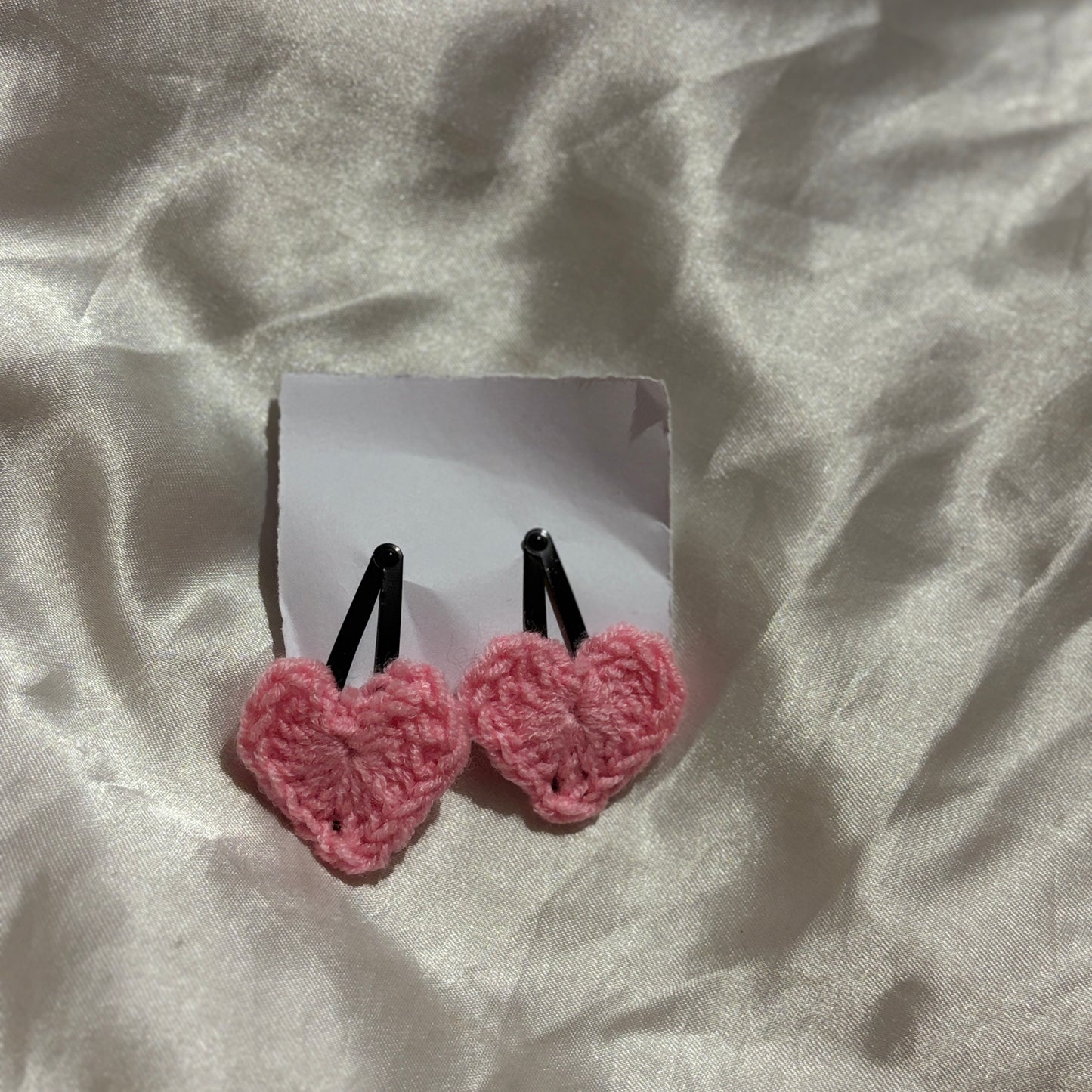 Pink heart-shaped earrings on a white card against a textured beige background