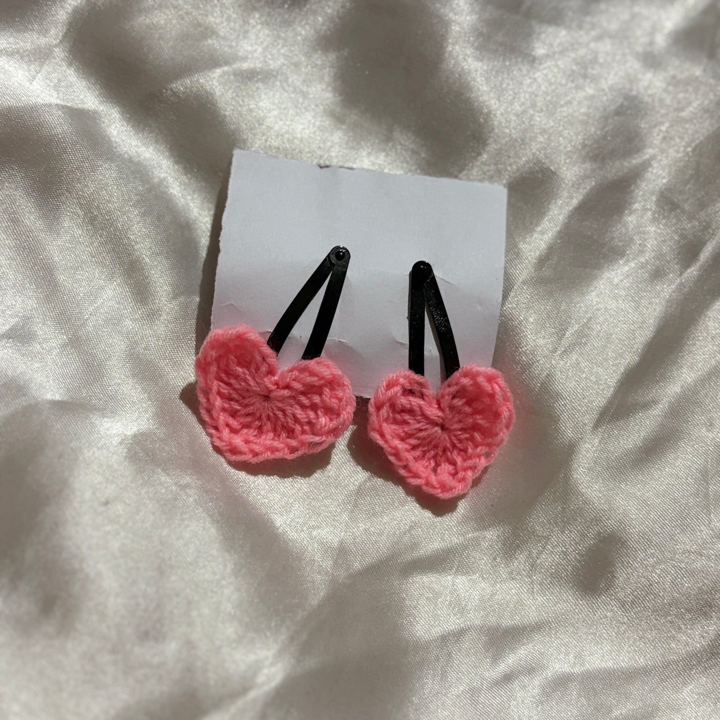 Pink heart-shaped hair clips on a white card with a light fabric background