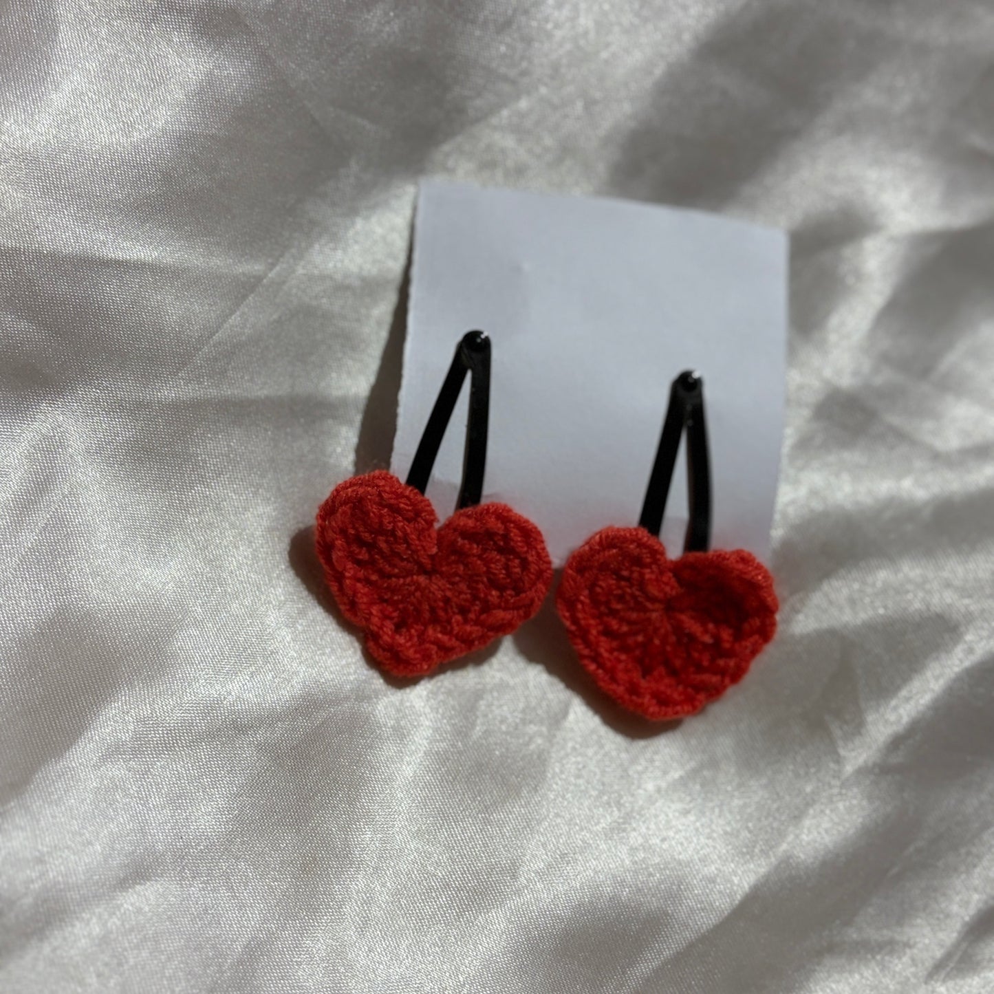 Red heart-shaped earrings on a white card with a silver fabric background
