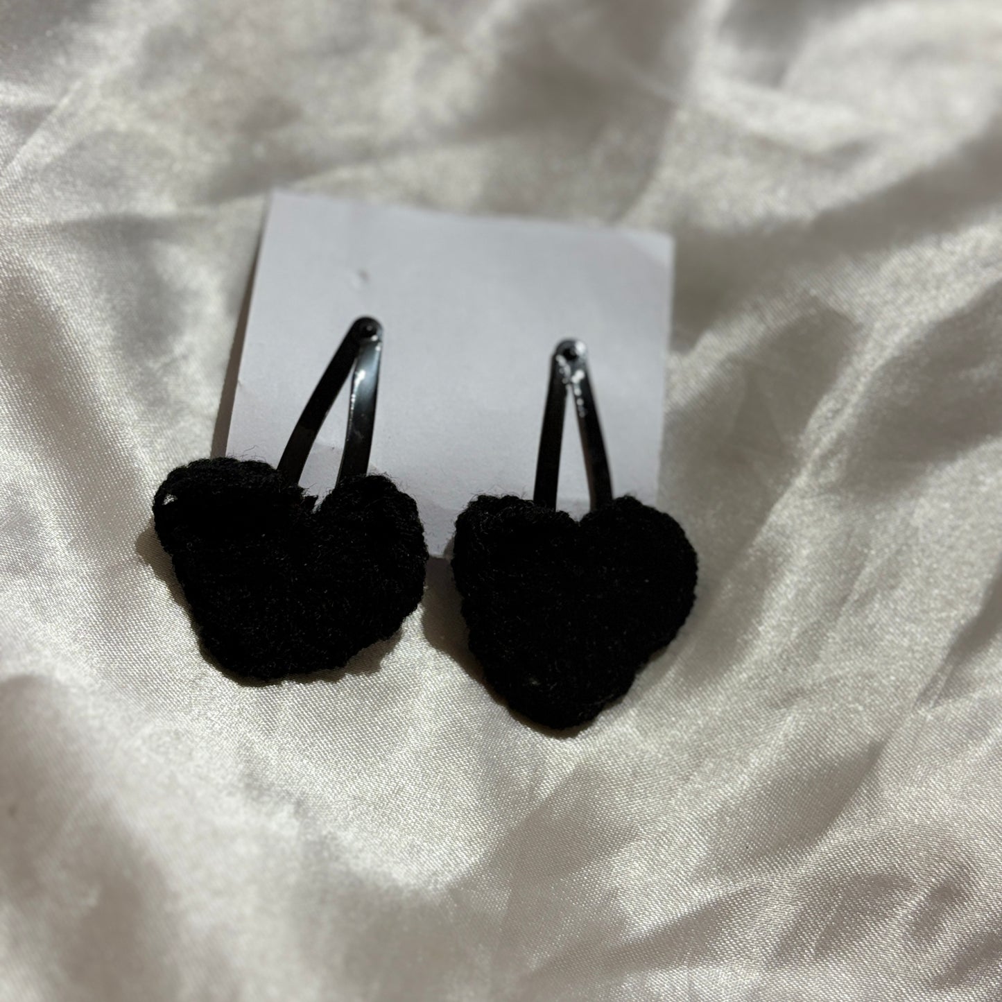 Black heart-shaped earrings on a white card with a white fabric background