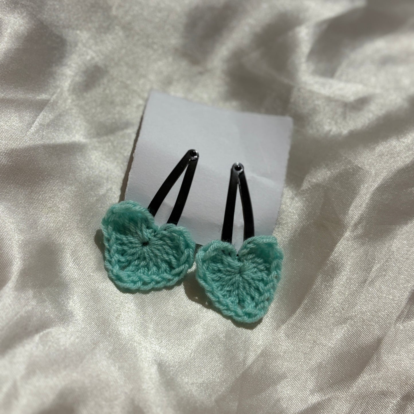 Two turquoise butterfly-shaped hair clips on a white card with a light fabric background