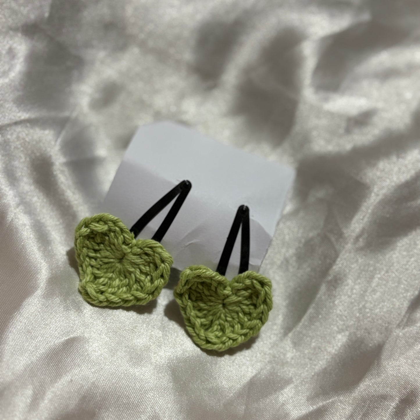 Two green crochet hair clips on a white fabric background