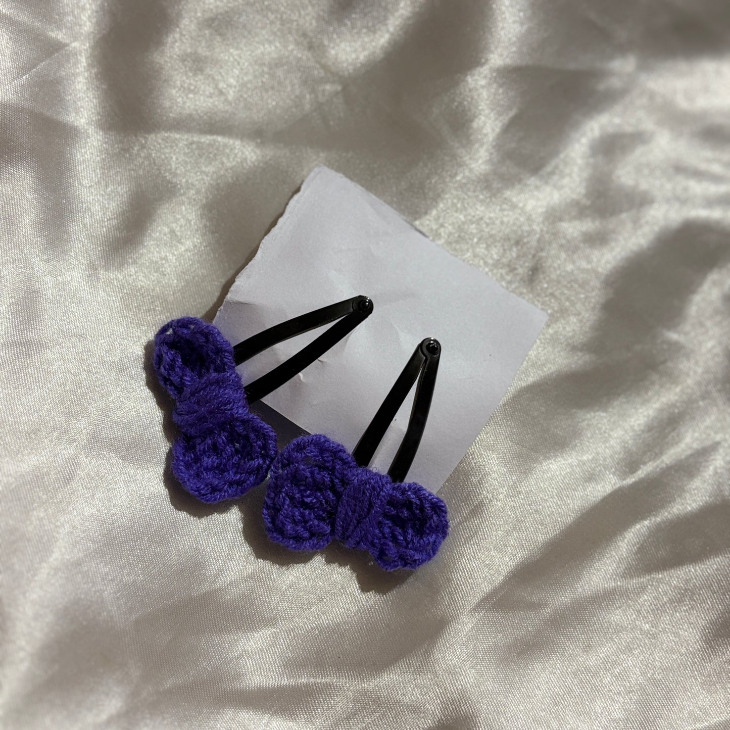 Two purple hair clips on a white card with a textured white background