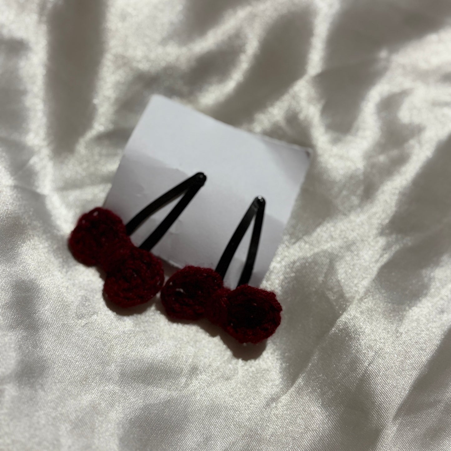 Two dark red hair clips on a white card with a light fabric background