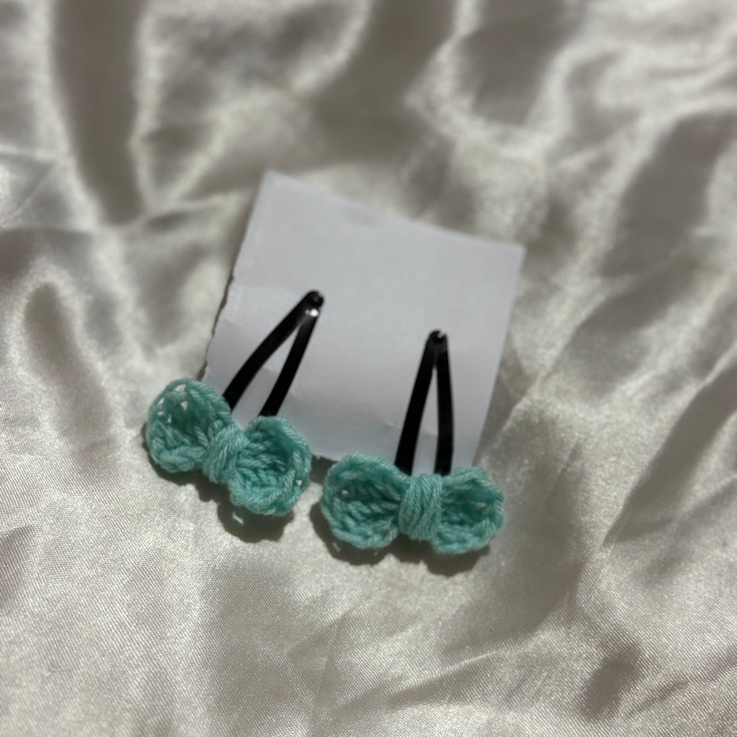Two light blue hair ties with black ribbons on a white card, placed on a textured beige fabric background.