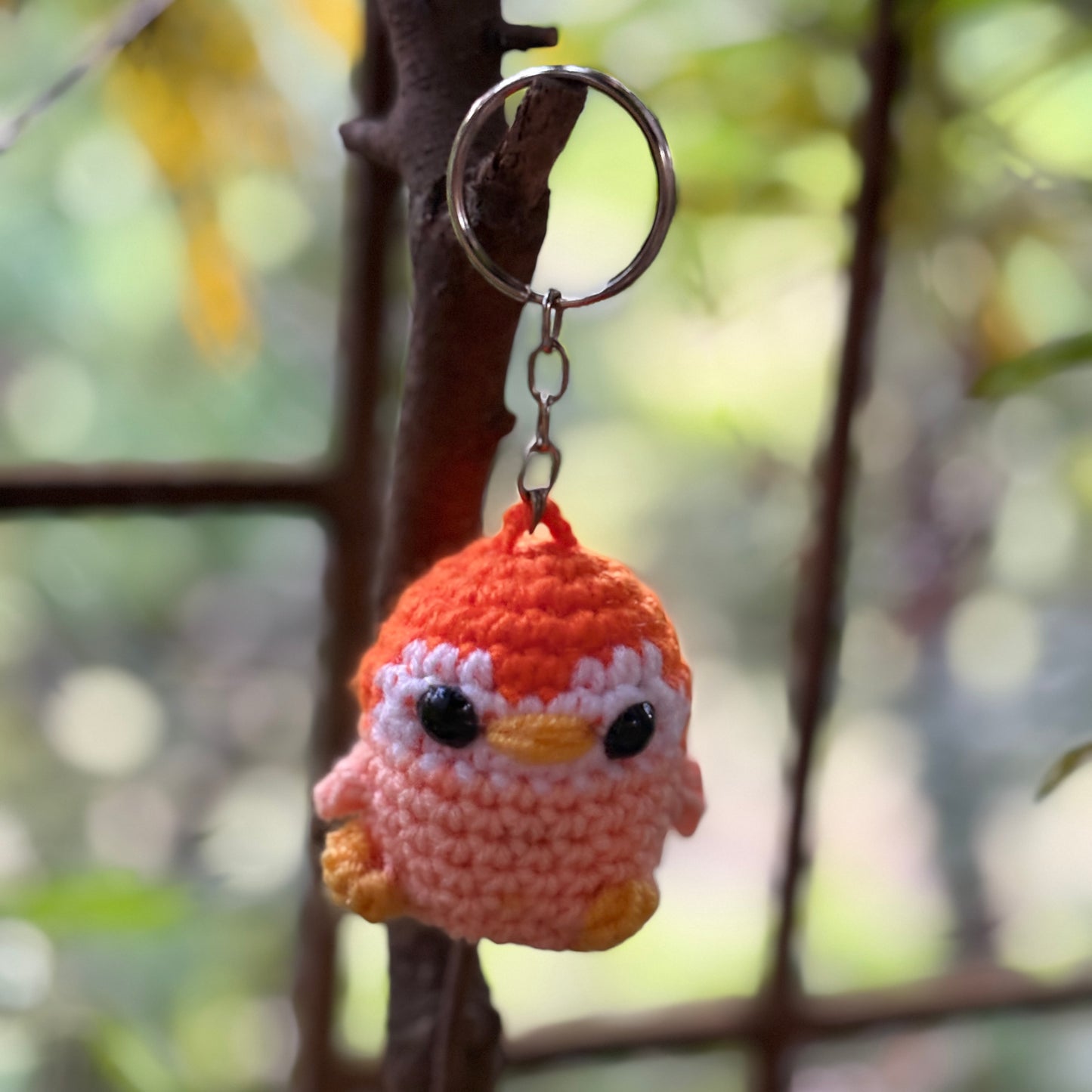 Crocheted penguin keychain hanging on a branch with a blurred natural background