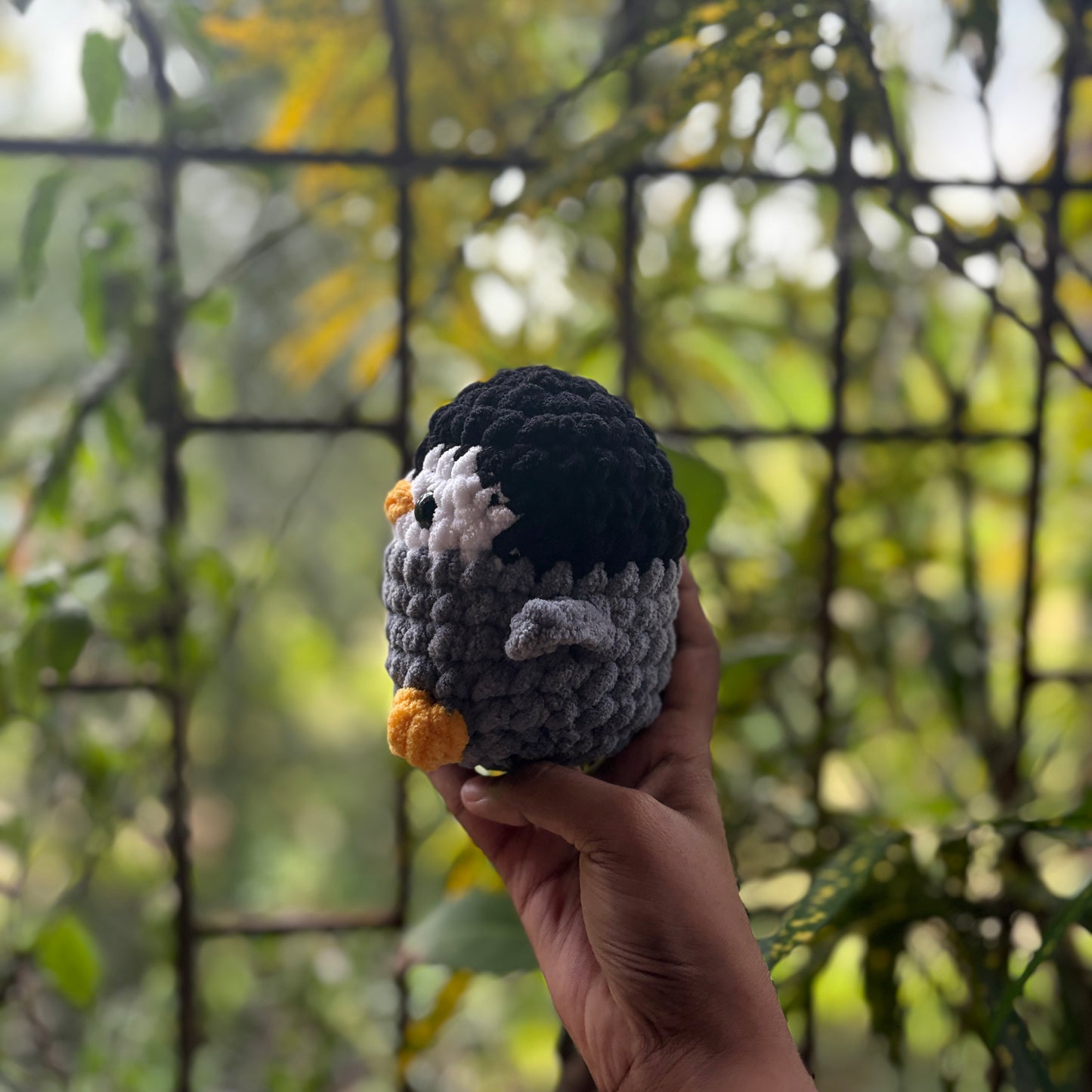 Hand holding a small crochet penguin toy with a blurred natural background