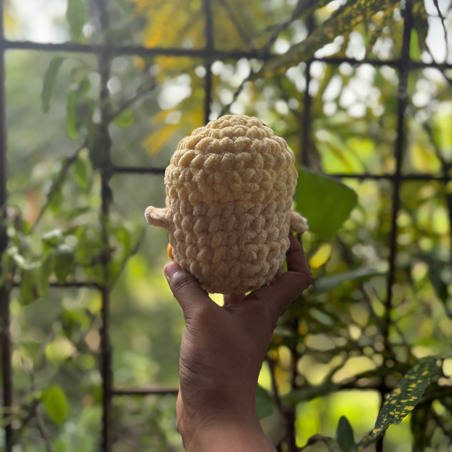 Hand holding a small crochet penguin toy with a blurred natural background
