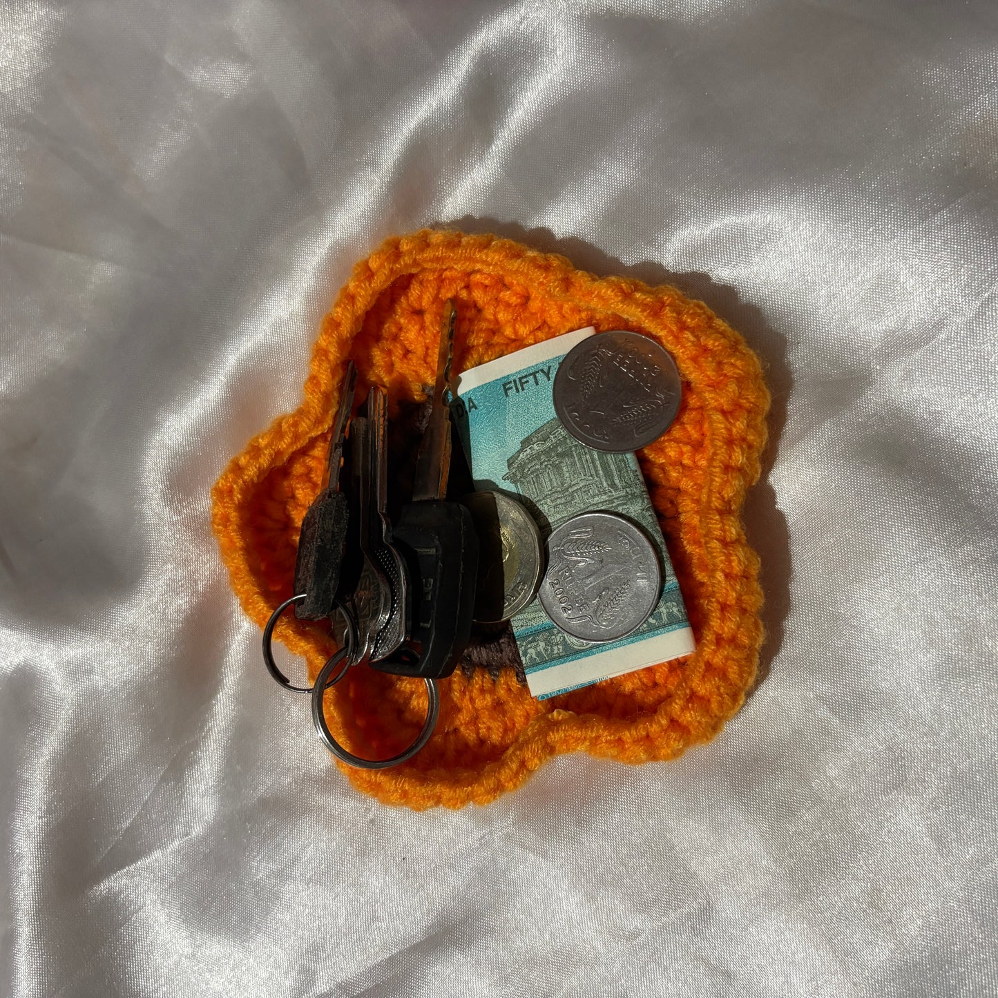 Orange crochet coin purse with keys and money on a white fabric background