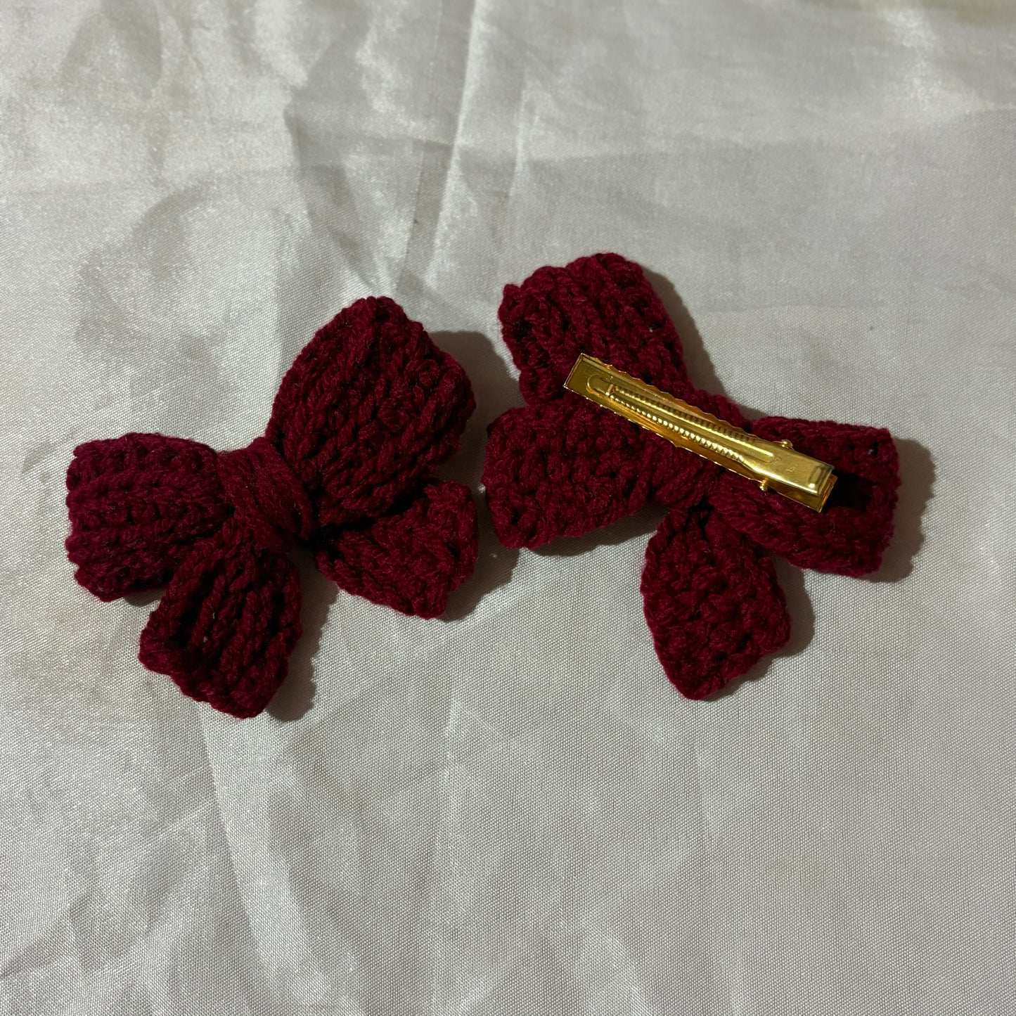 Two red crochet bow hair clips on a white fabric background