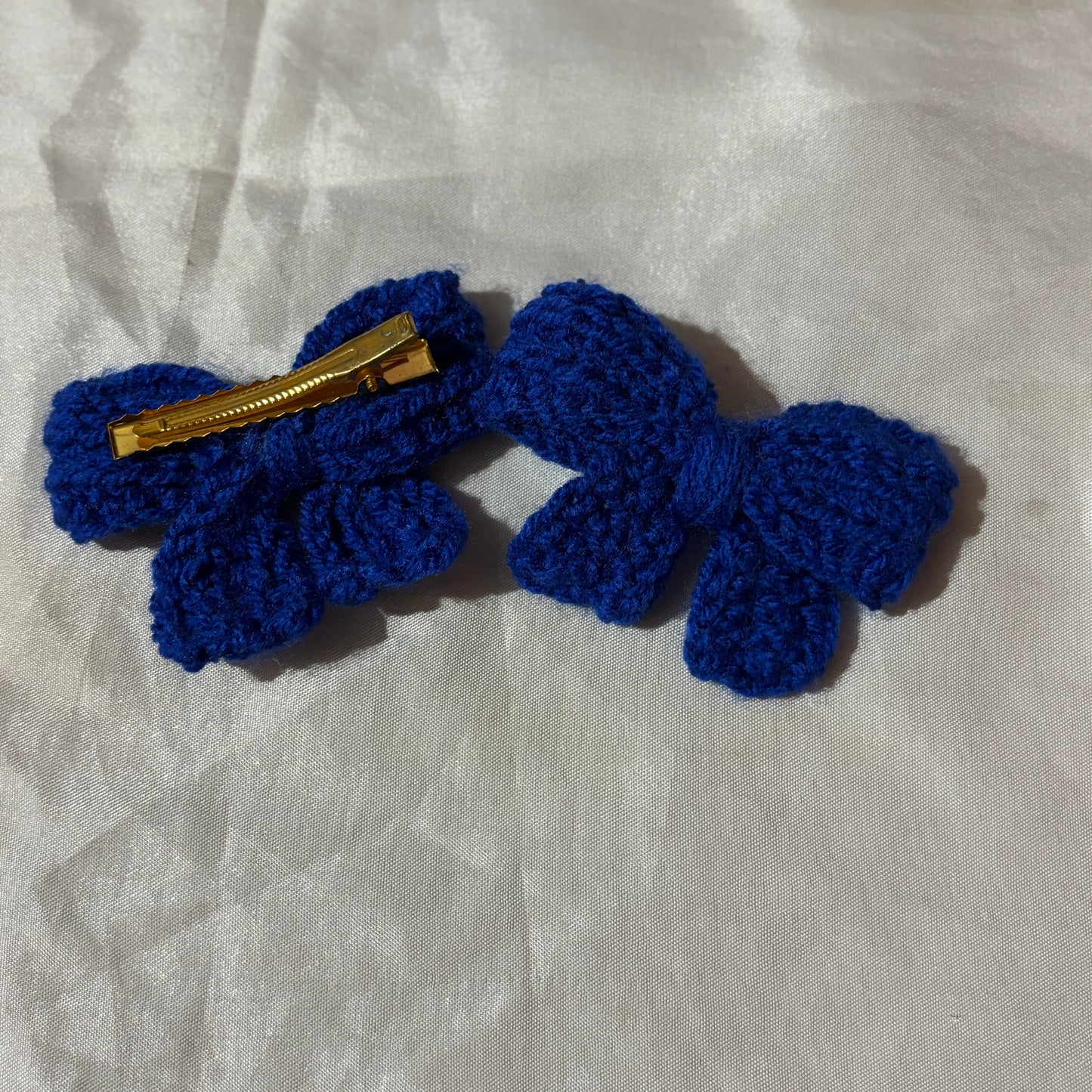 Blue crocheted bow clips with a gold clip on a light gray fabric background