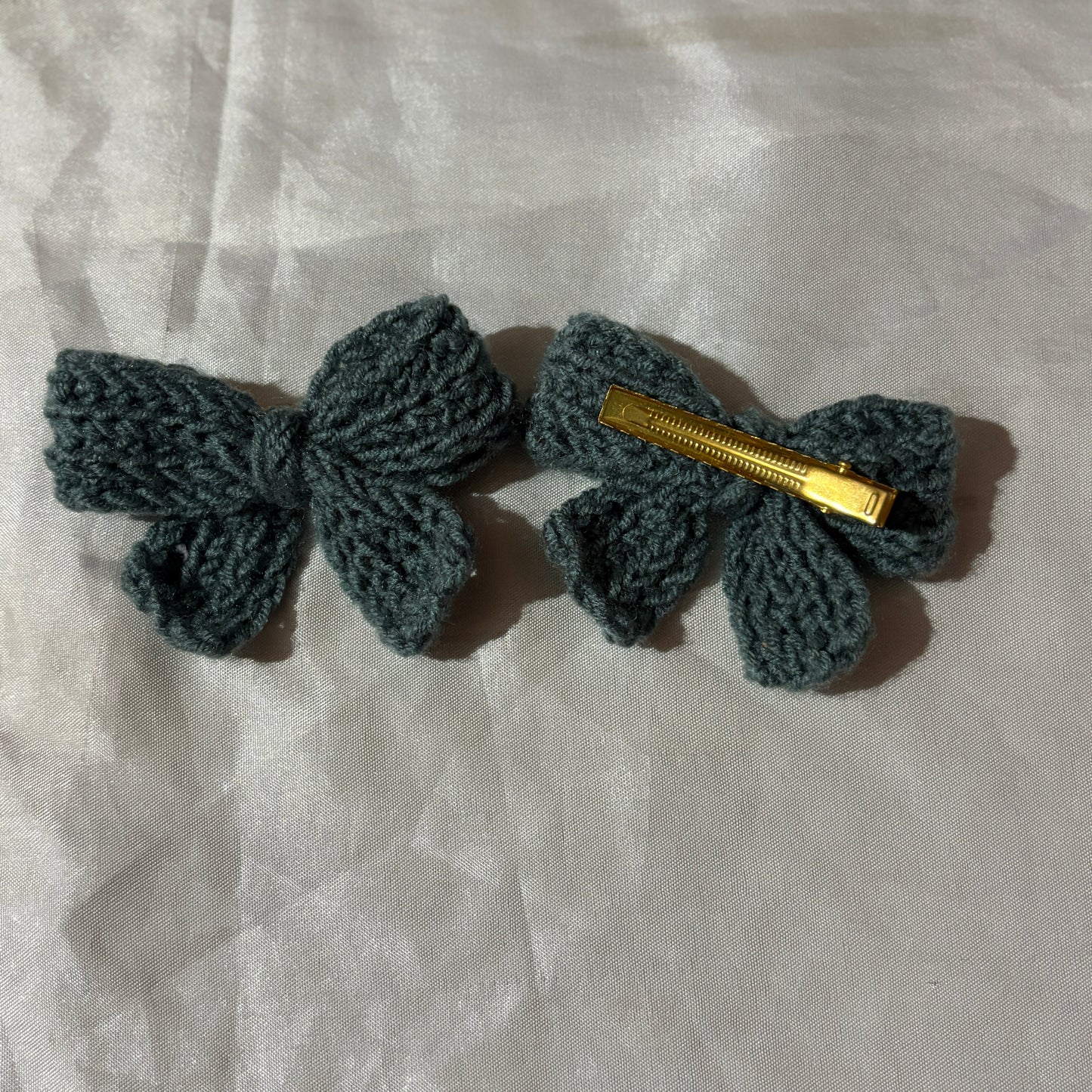 Two crocheted hair bows with gold clips on a light fabric background
