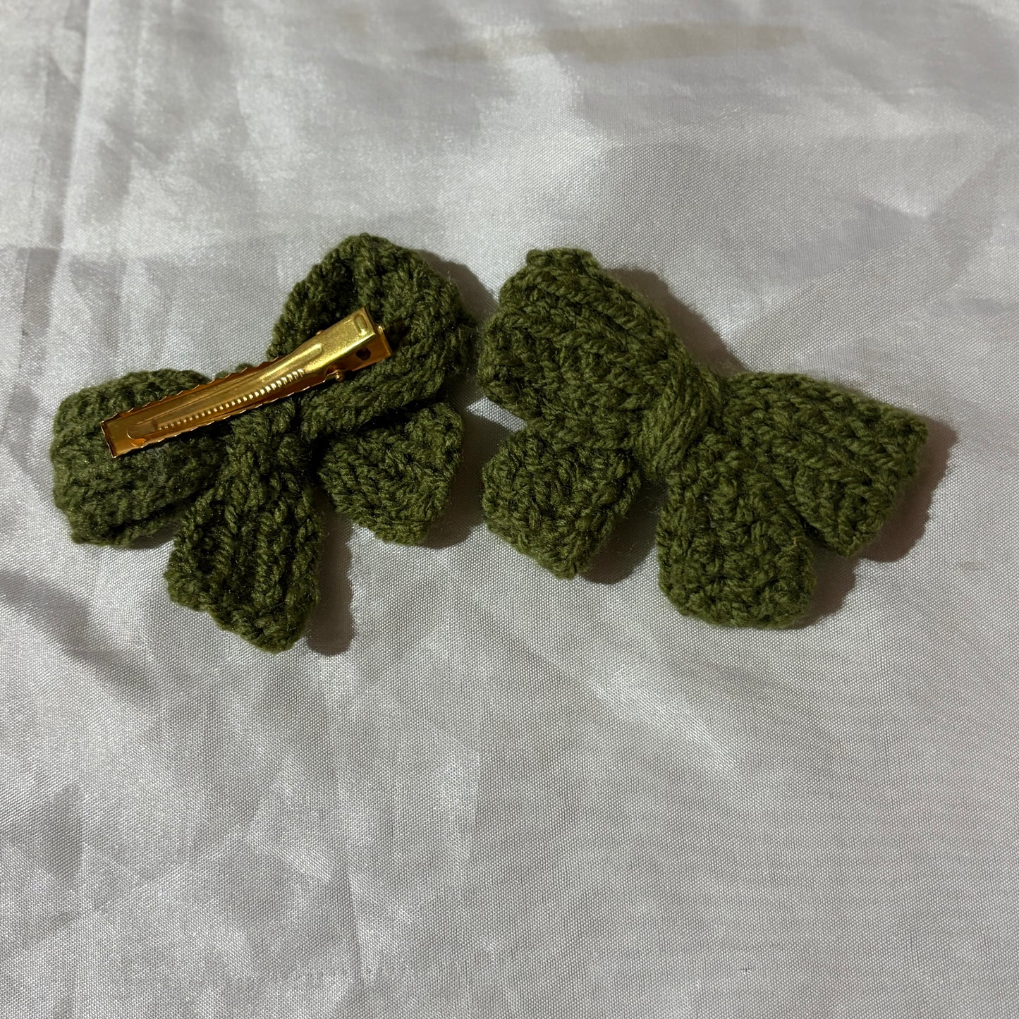 Green crocheted hair clips on a white fabric background