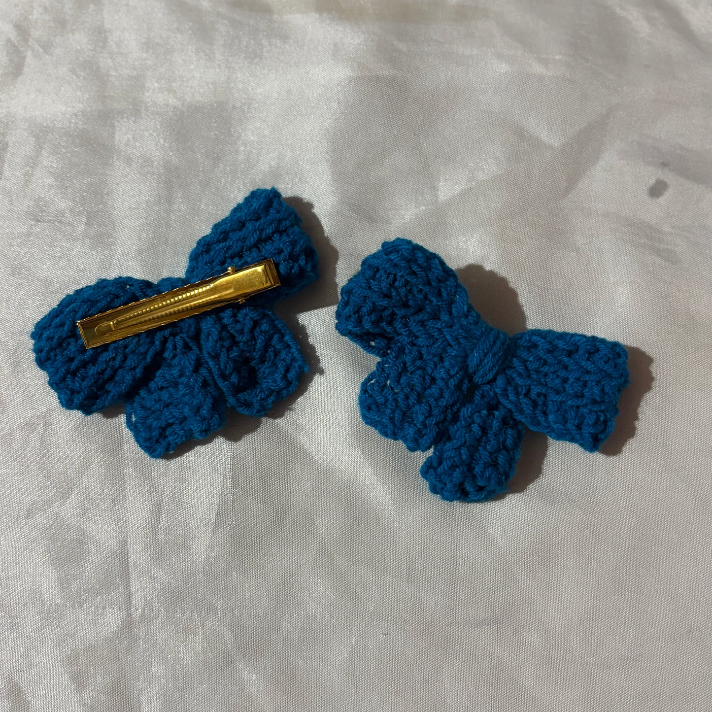 Two blue crocheted hair bows on a textured white background