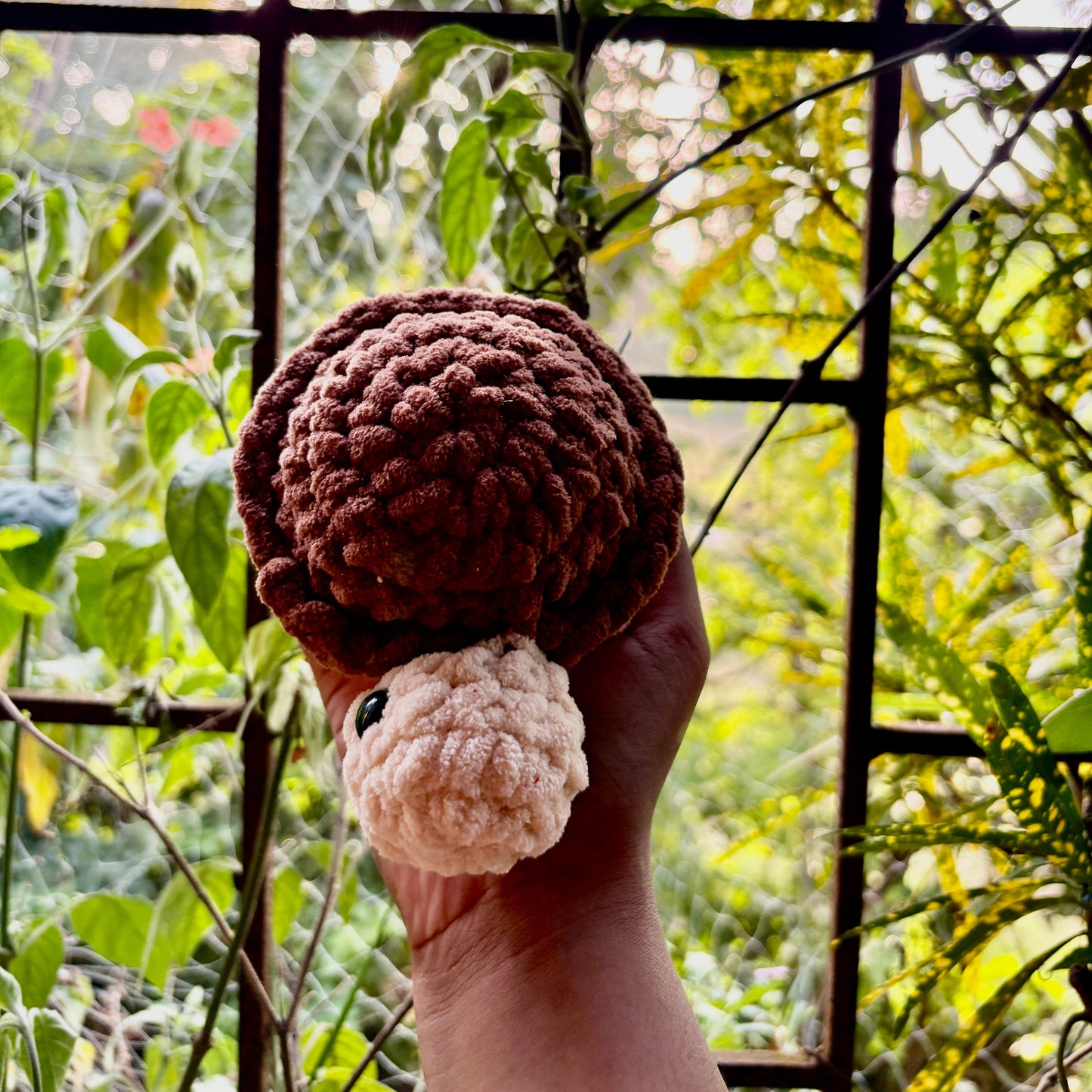 Hand holding a small crocheted turtle with a purple shell against a natural background