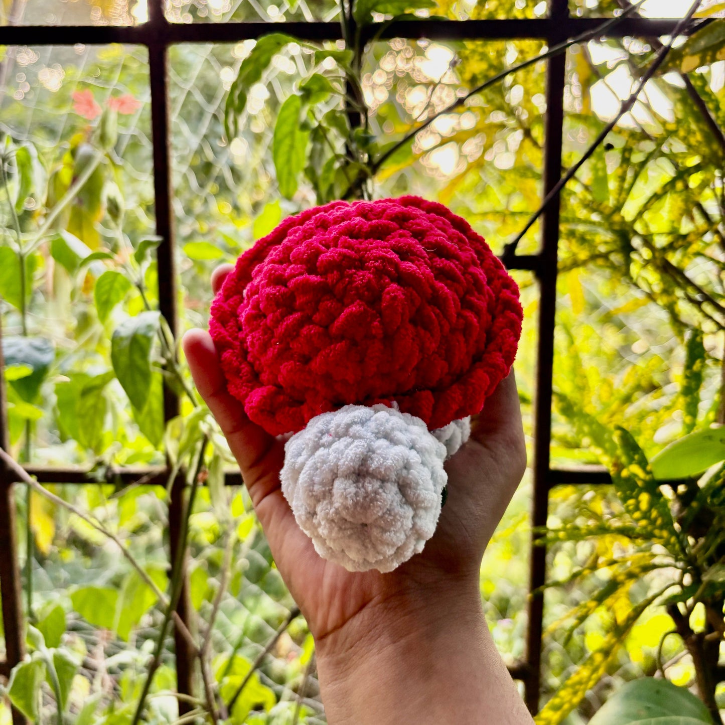 Hand holding a small crocheted turtle with a red shell against a natural background