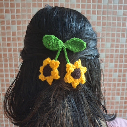 Person with black hair wearing a green and yellow crocheted hair flower accessory against a tiled wall.