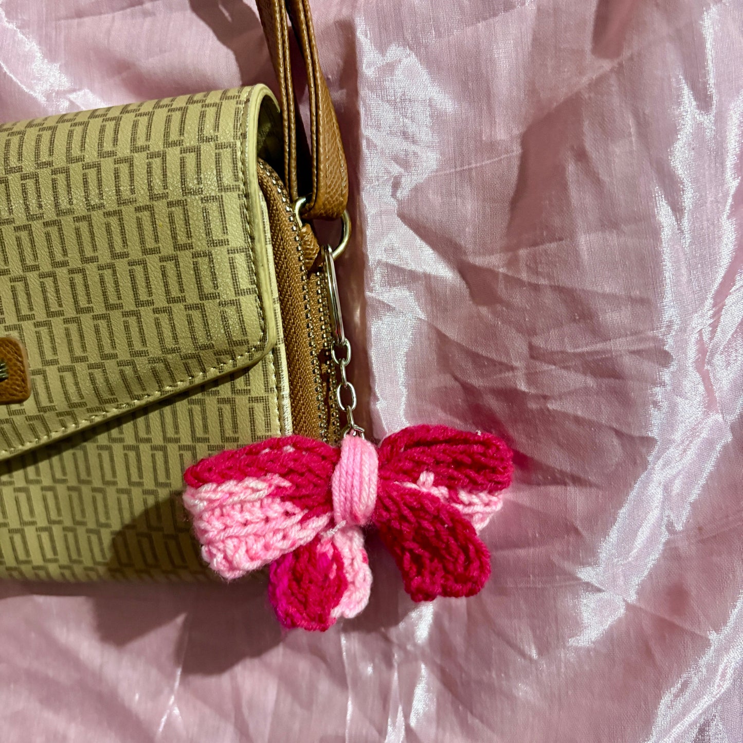 Green textured handbag with a pink and red bow charm on a light pink fabric background